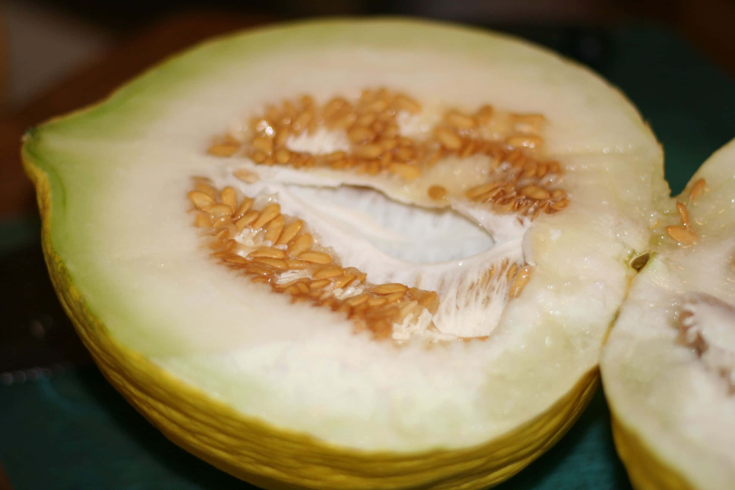 帶籽的黃色卡薩巴瓜切片 壁紙 — 半個蜜瓜的特寫，露出其淡色果肉和一簇琥珀色的種子。