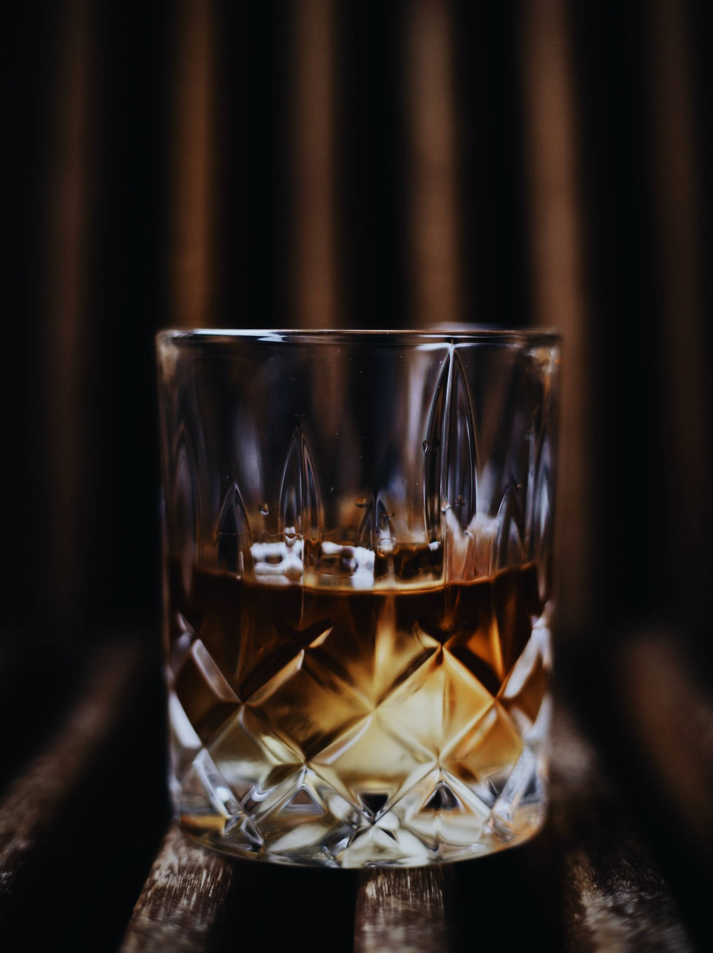 一個切割水晶威士忌杯，盛載著琥珀色液體，放在昏暗光線下的木桌上。