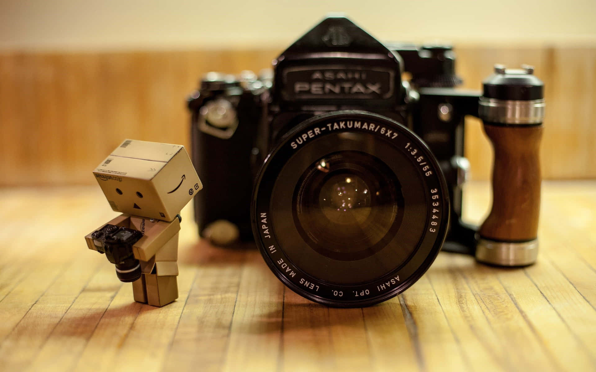 紙板Danbo玩具喺復古Pentax相機旁邊揸住相機，喺木地板上。