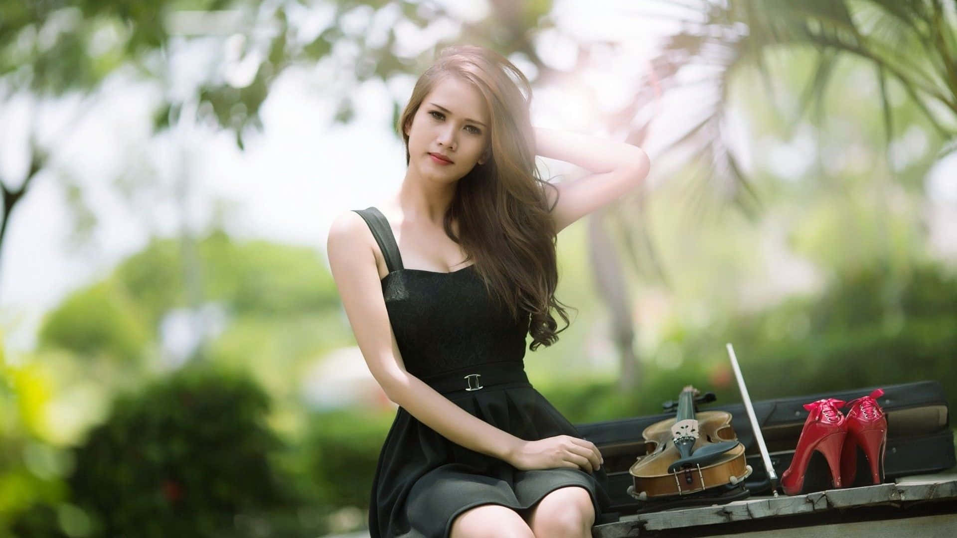 帶著淡淡微笑的美麗年輕女子 壁紙 — 一位身穿黑色連衣裙的女性坐在戶外的長椅上，旁邊放著小提琴和紅色高跟鞋，沐浴在柔和的陽光中。
