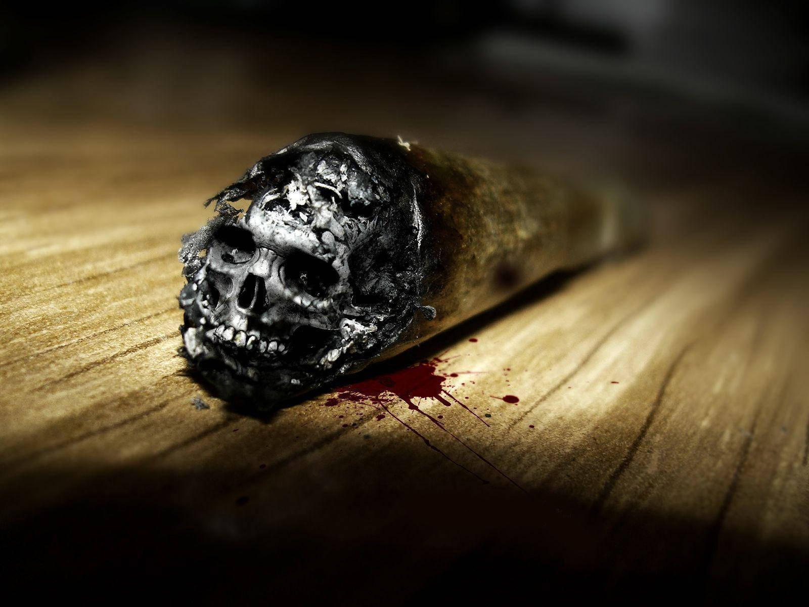 帶血跡的煙草高清骷髏 壁紙 — 一根燒焦的香煙，煙灰呈頭骨形狀，放在沾有紅色飛濺物的木質表面上。