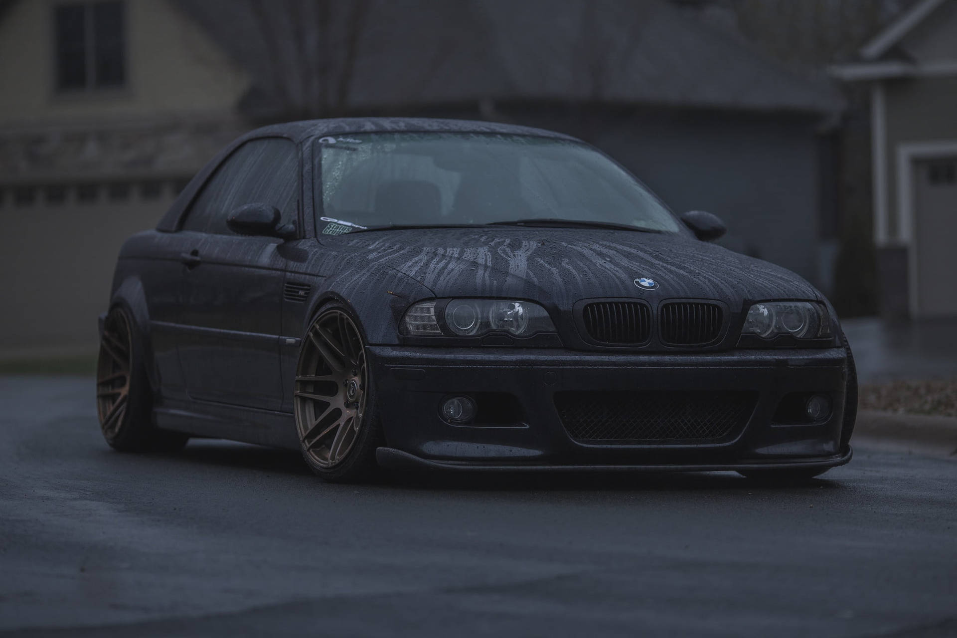 黑色BMW M3雙門轎跑車，金色輪圈，停在潮濕街道上，暮色中。