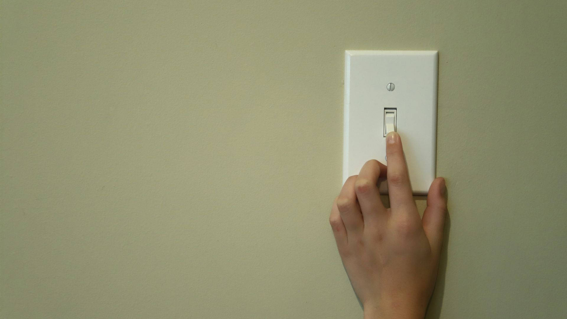 常見美國式燈開關 壁紙 — 一隻手在簡單的室內環境中按下米色牆上的白色燈掣。