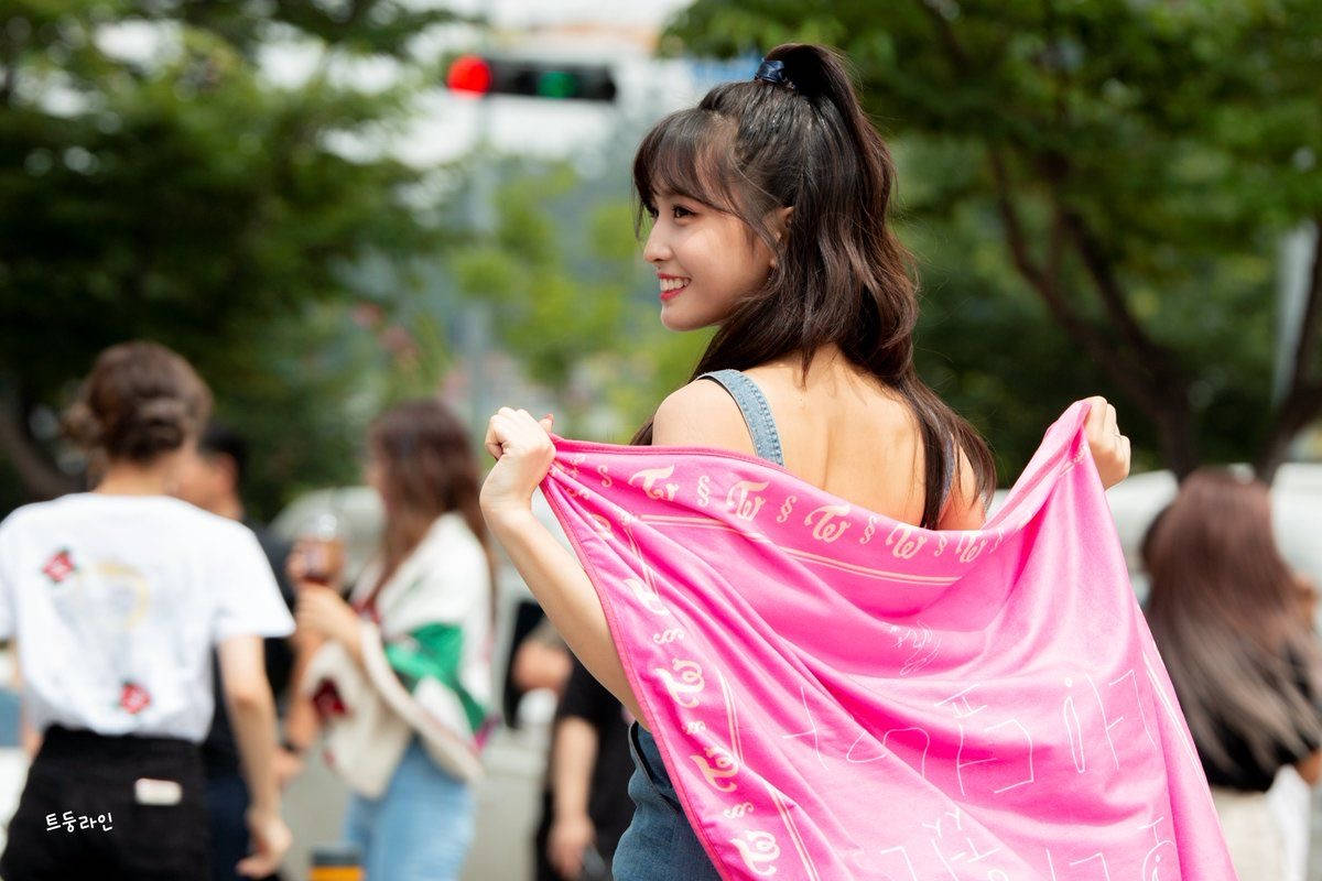 年輕女子微笑著在城市街道上舉起一條粉色圍巾。
