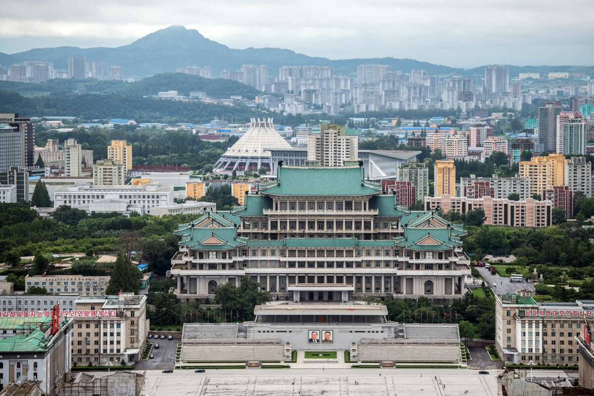 在密集的城市區域中，一座擁有綠色屋頂的大型傳統建築，背景是山脈。