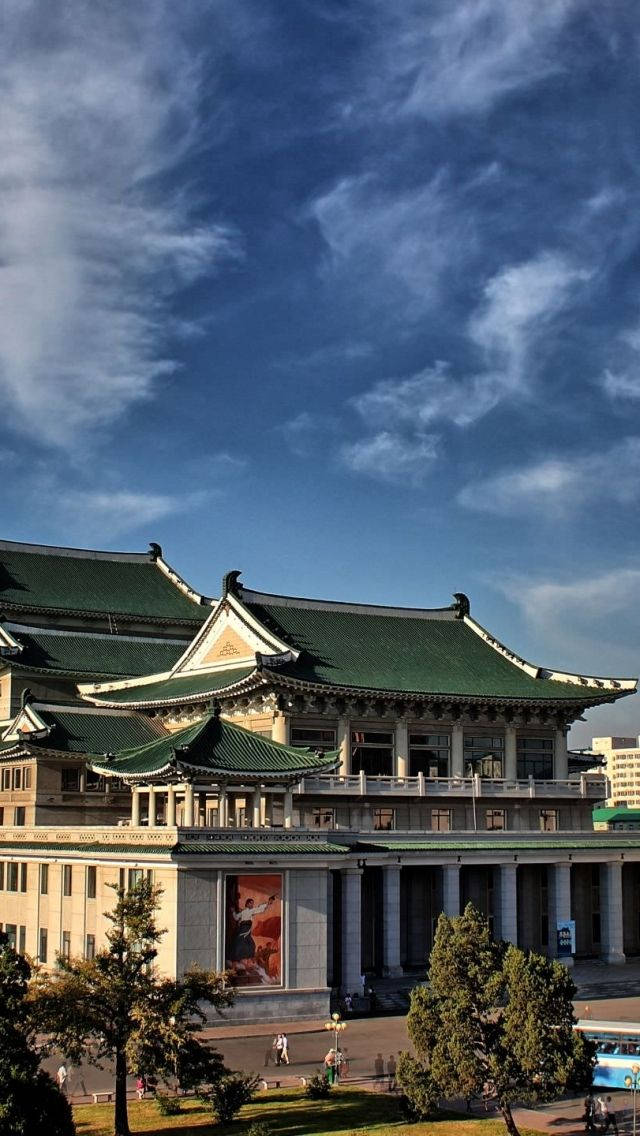 宏偉的傳統建築，擁有綠色屋頂，在明亮的藍天和散落的雲朵下。