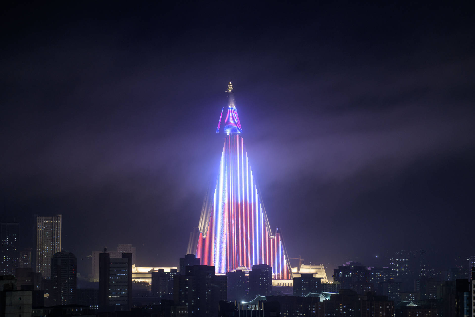 夜晚一座明亮照明的金字塔形建築，背景是城市天際線。