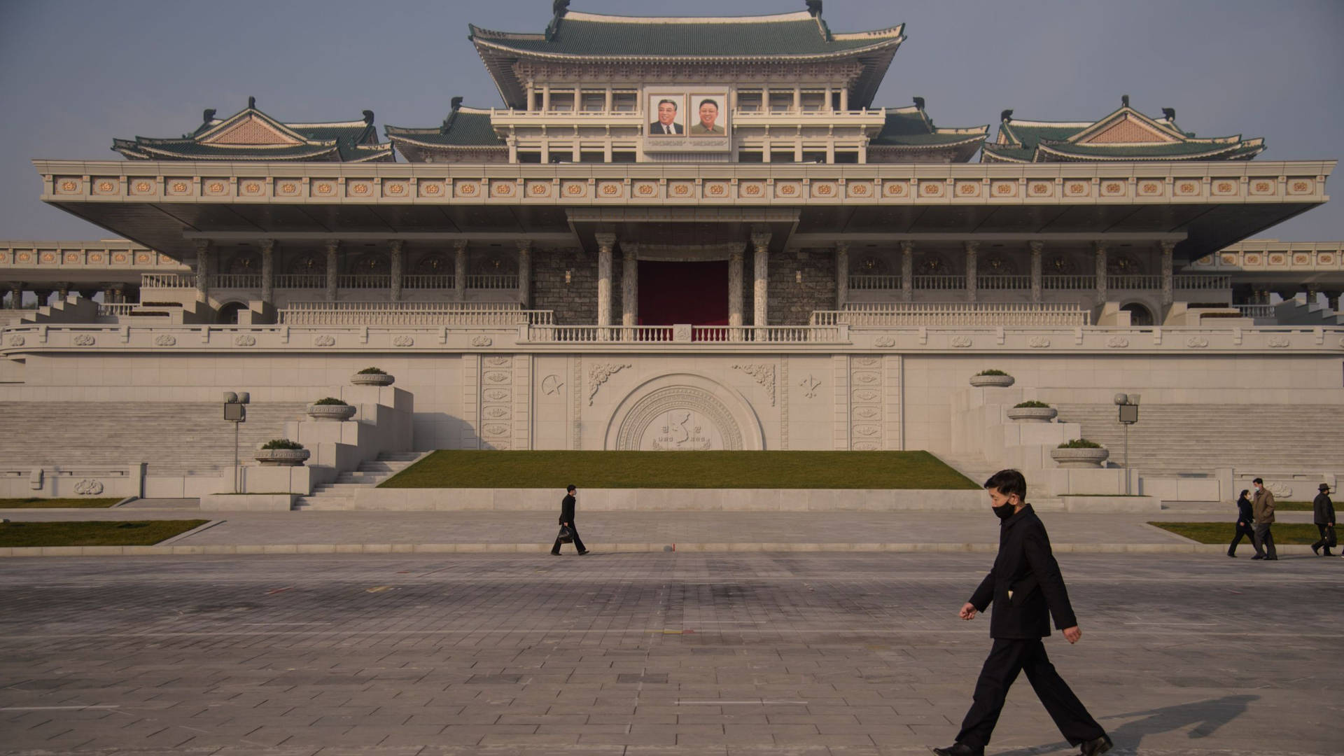人們在一座大型政府建築前行走，入口上方有肖像。