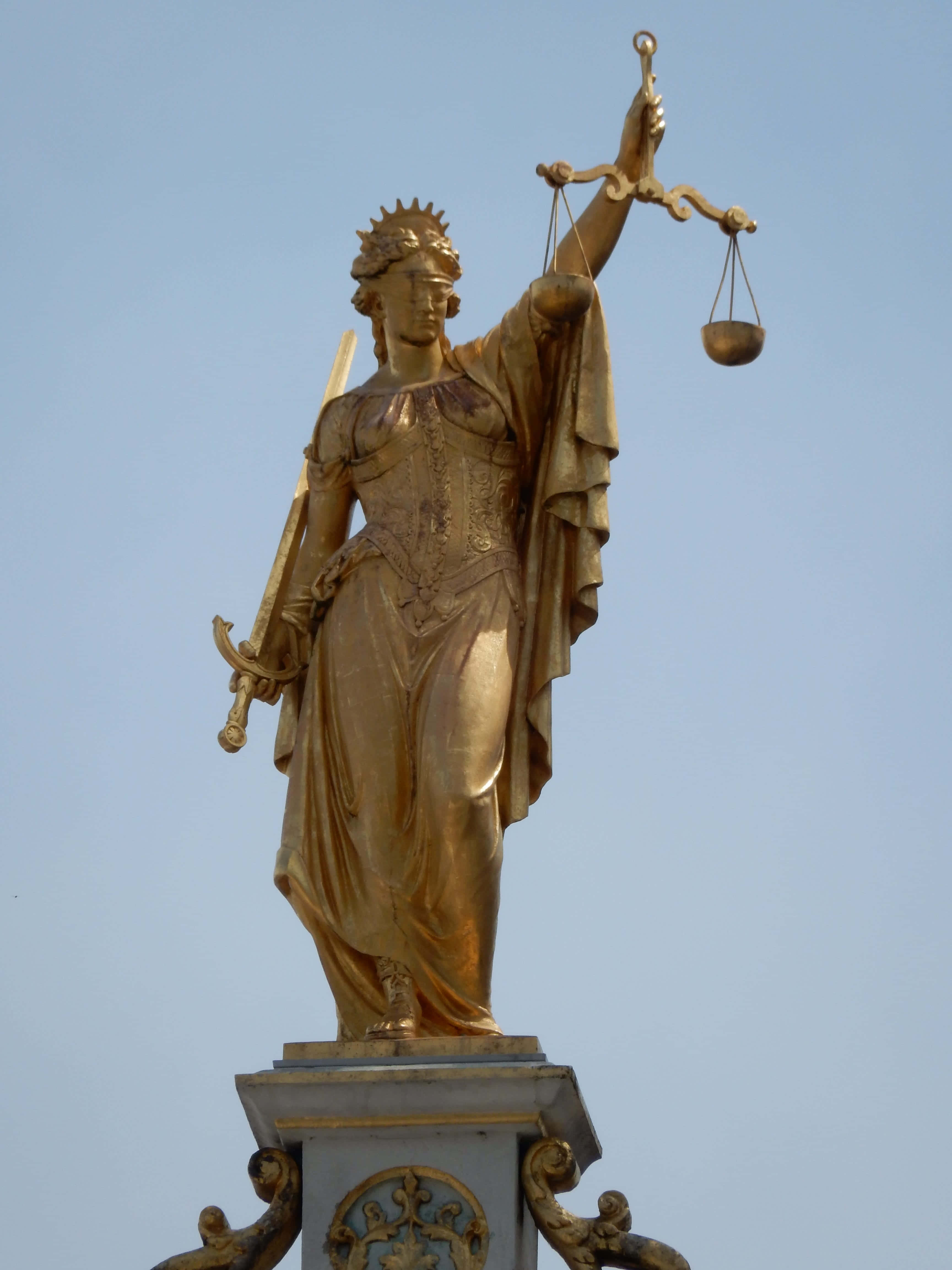 平等主義的正義女神雕像 壁紙 — 金色正義女神雕像，手持天秤與劍，以清澈藍天為背景。