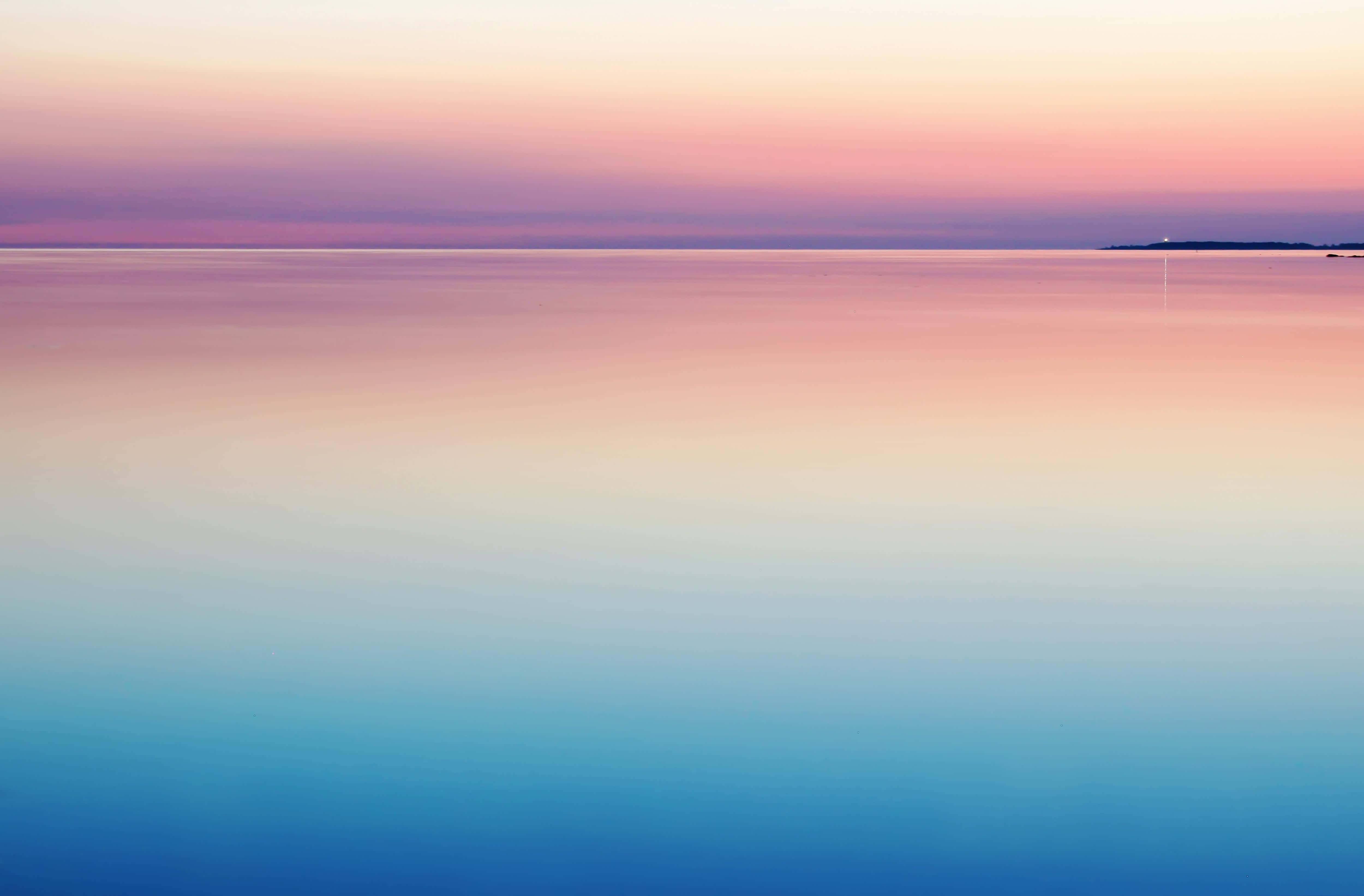 Minimalist Sunset 桌布 壁紙 — 平靜水面上寧靜的日落，柔和粉紅、紫色和藍色漸變融入寧靜的地平線。