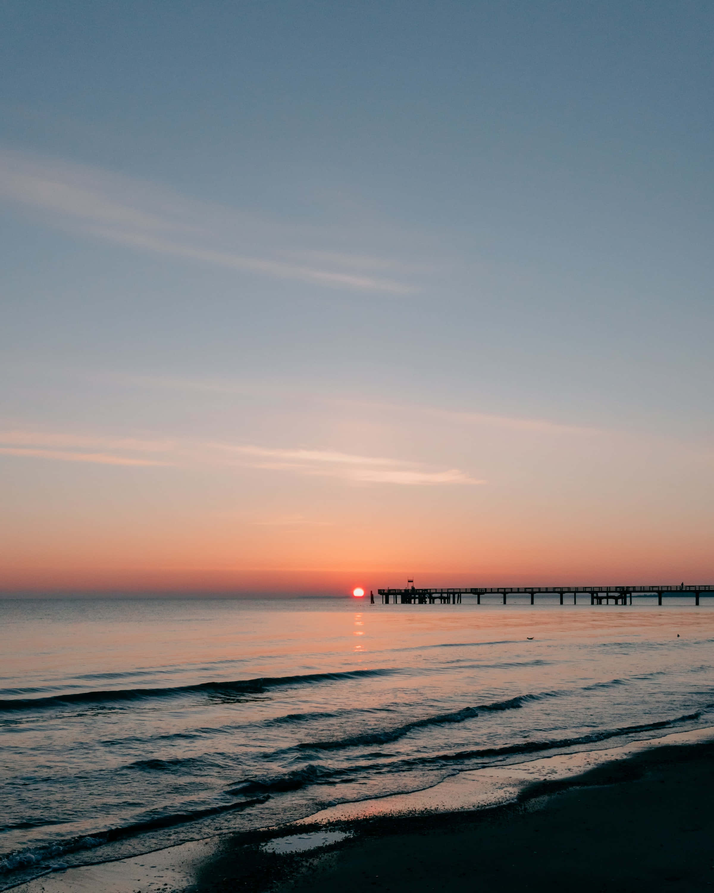 Sunset View 桌布 壁紙 — 平靜的日落映照在平靜的海面上，一條長長的碼頭在漸變的天空下延伸至地平線。