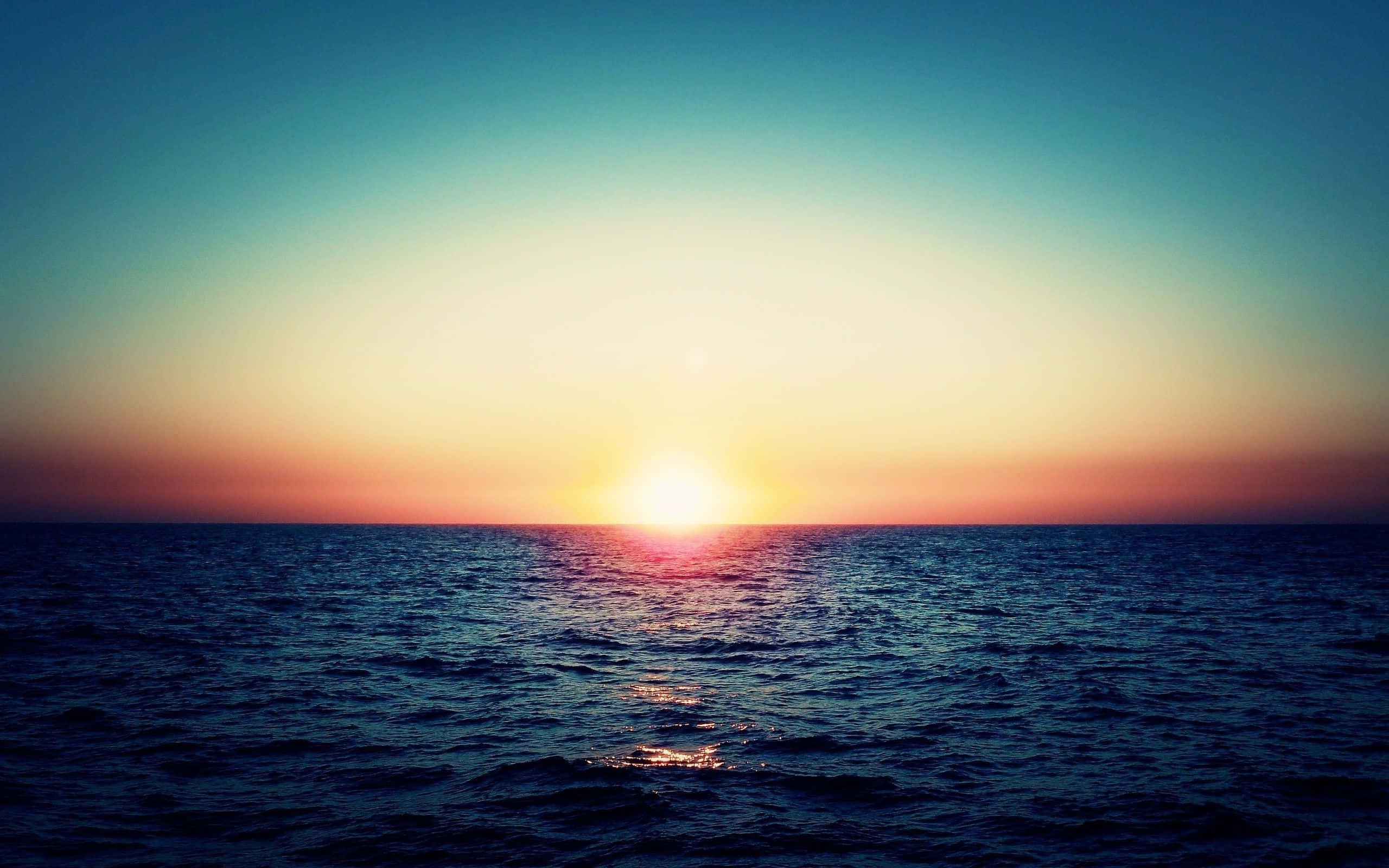 Sunset Ocean 桌布 壁紙 — 平靜的海面上，夕陽西下，金色的太陽沉入地平線，溫暖的光芒灑滿天空。