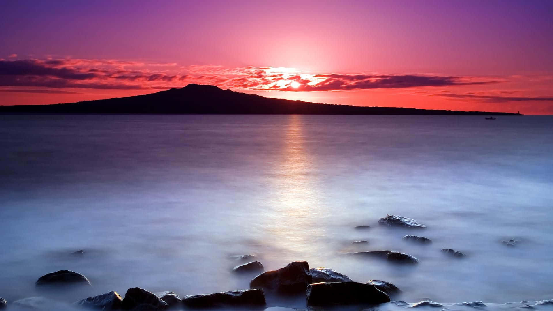 Purple Sunset 桌布 壁紙 — 平靜的海面上寧靜的日落，遠山的輪廓和發光的紫橙色天空。