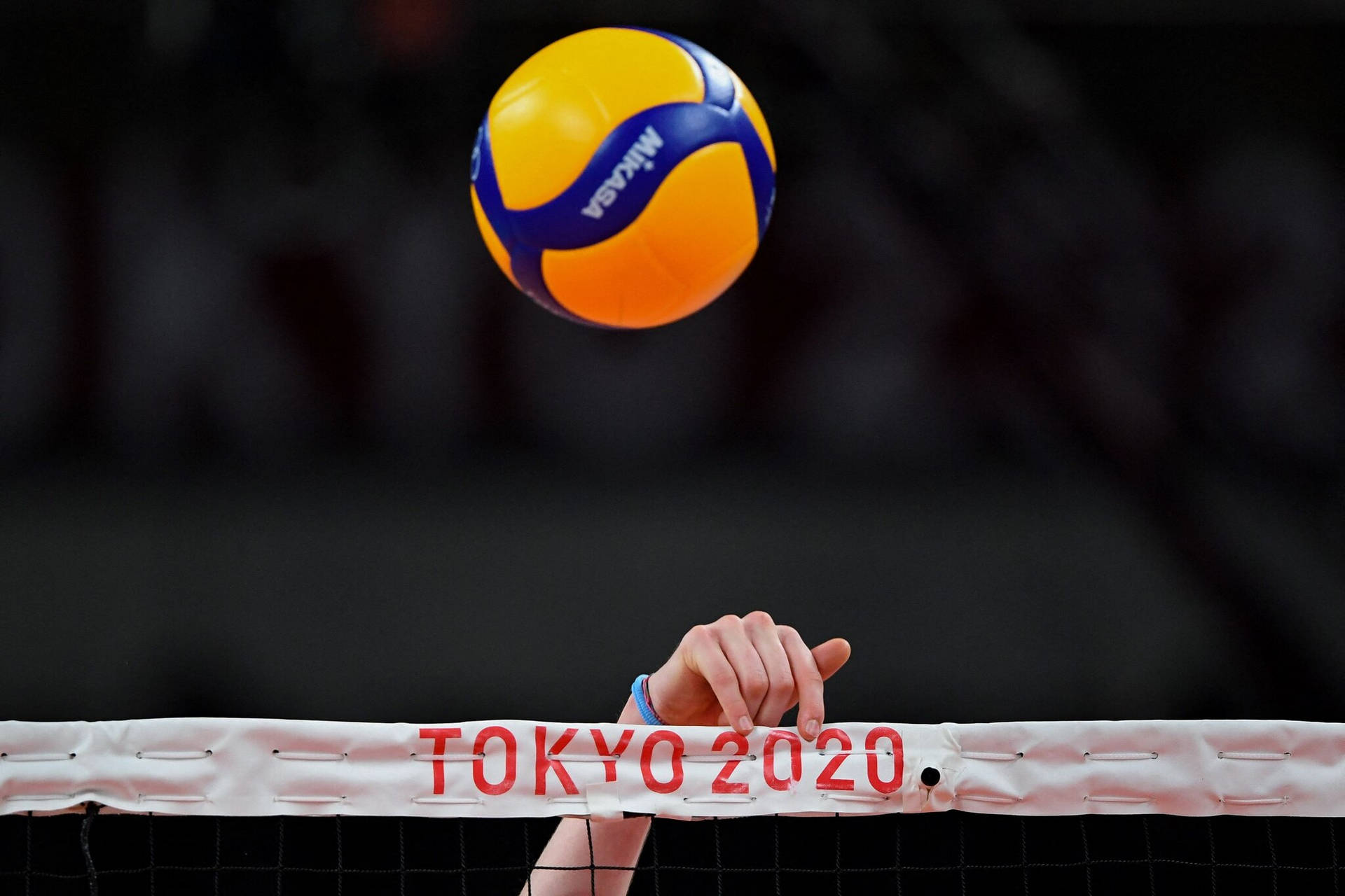 一隻手抓住標有 Tokyo 2020 的排球網，一個球懸浮在網上。