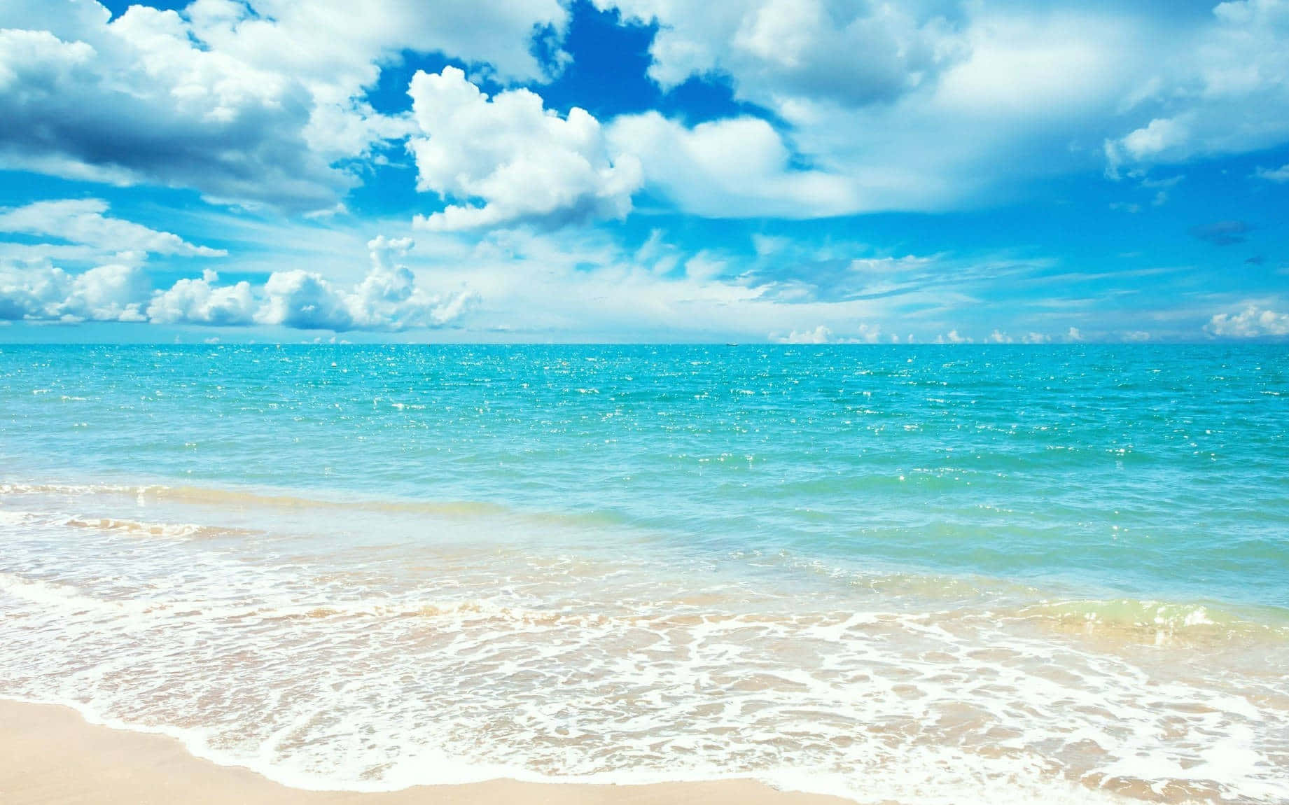 碧綠的海浪在明亮的藍天白雲下沖刷著金色的沙灘。