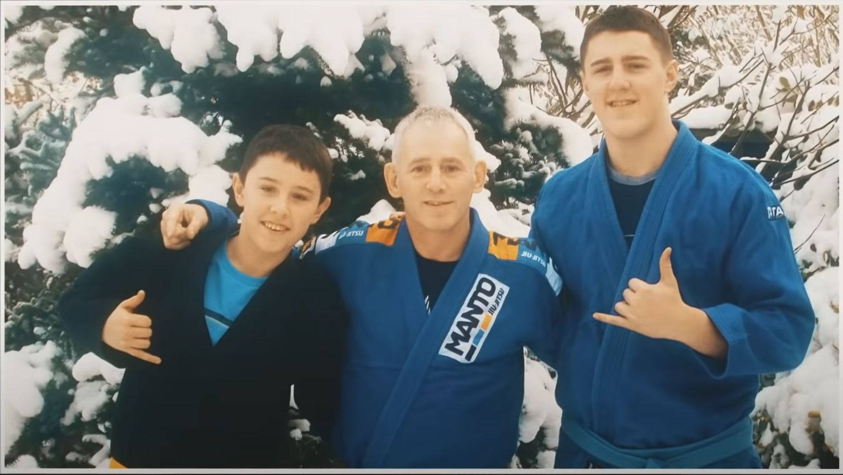 三名身穿柔道服的男子在雪地森林中微笑。