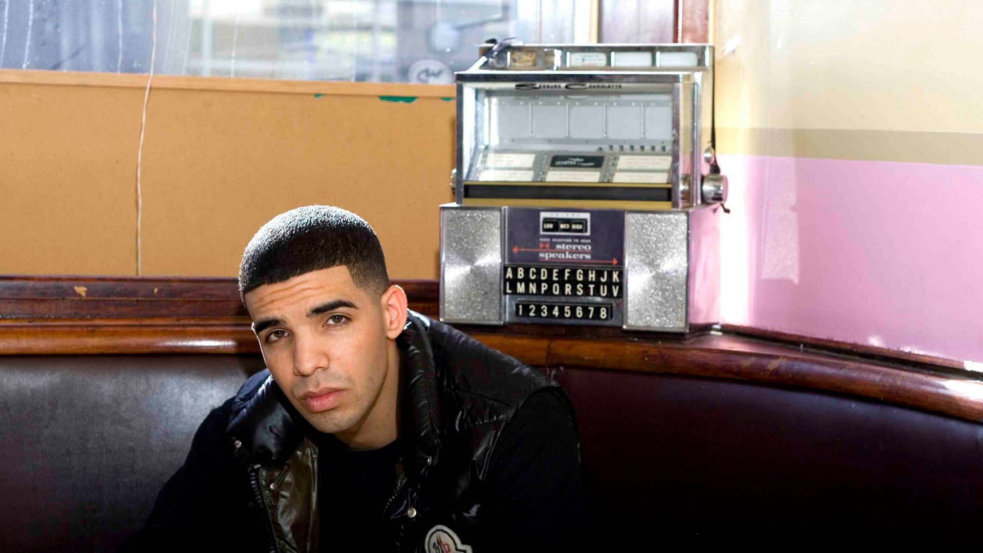Drake 在餐廳卡座旁，旁邊有一部懷舊點唱機。