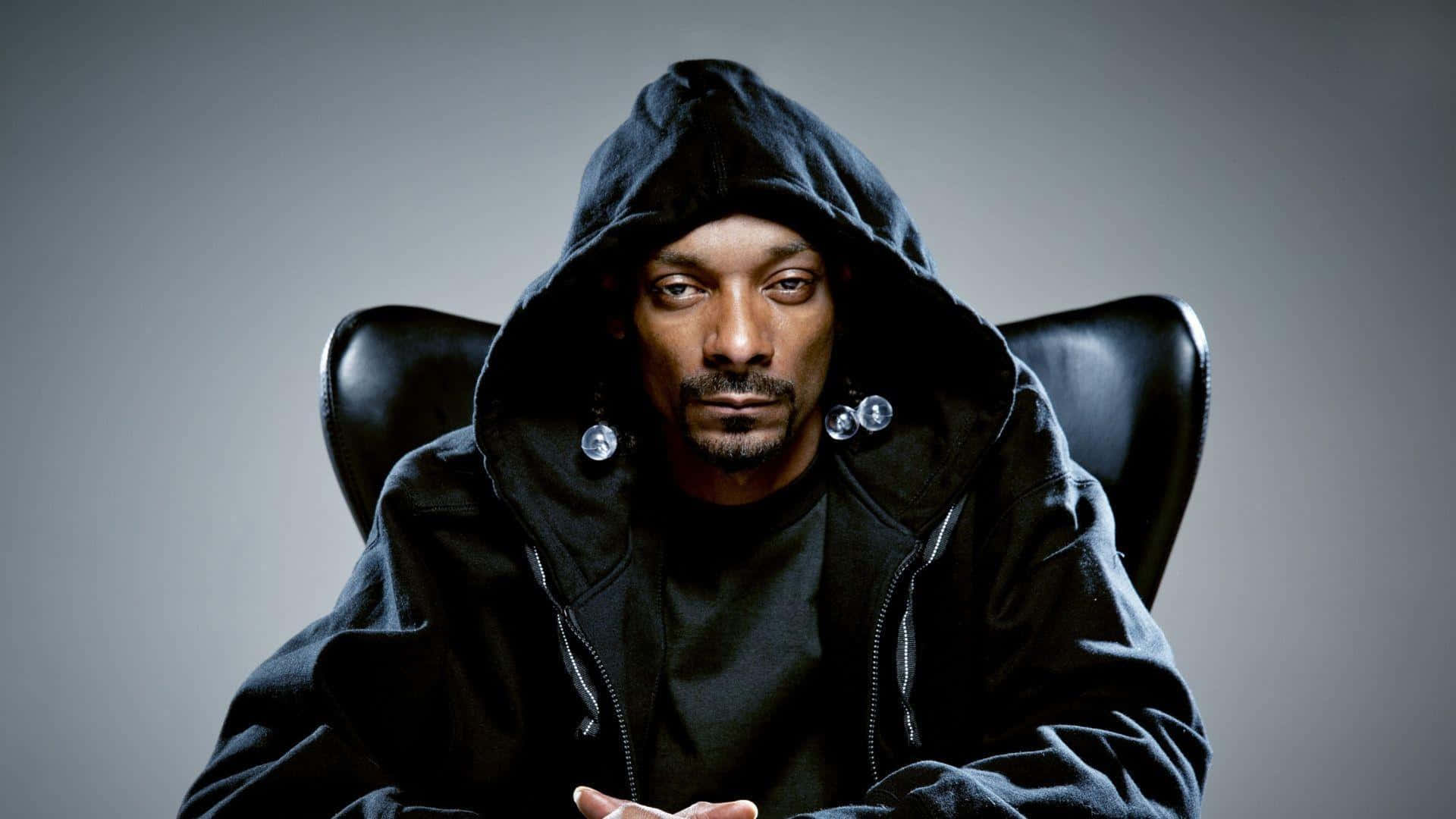 Snoop Dogg 身穿黑色連帽衫，戴著銀色耳環，坐在椅子上。