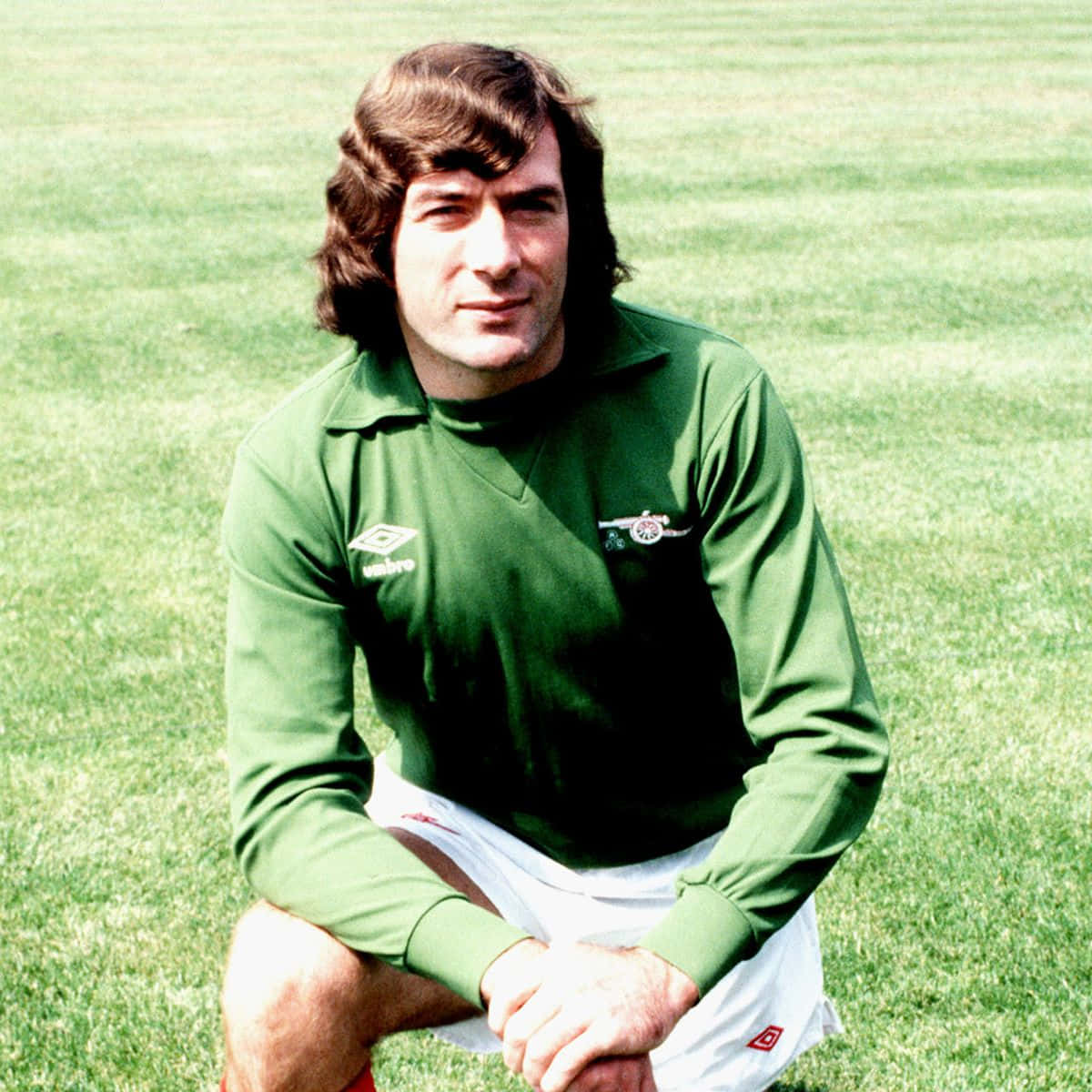 年輕的北愛爾蘭足球員 Pat Jennings 壁紙 — 一位身穿綠色長袖球衣的復古足球員，在修剪整齊的草地上自信地跪著。