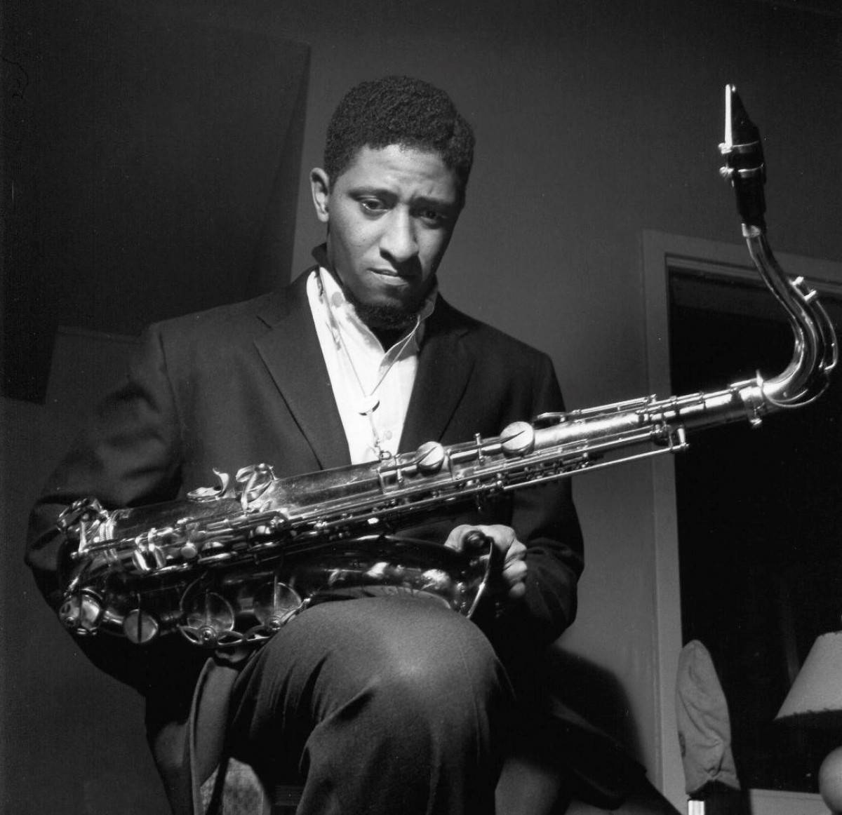 年輕的美國薩克斯風手 Sonny Rollins 壁紙 — 一個穿著西裝的男人在昏暗的房間裡專注地拿著色士風的黑白肖像。