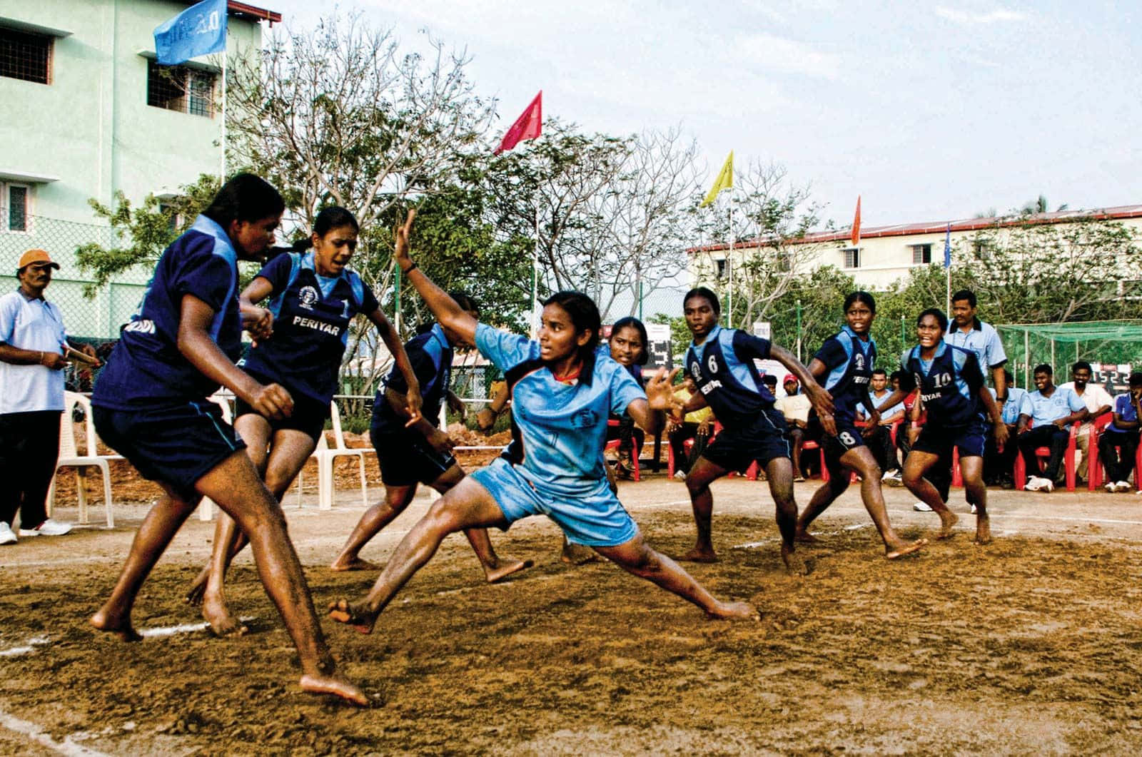 Kabaddi 桌布 壁紙 — 年輕運動員在明亮的日光下，在泥濘的場地上赤腳進行團隊運動，激烈競爭。