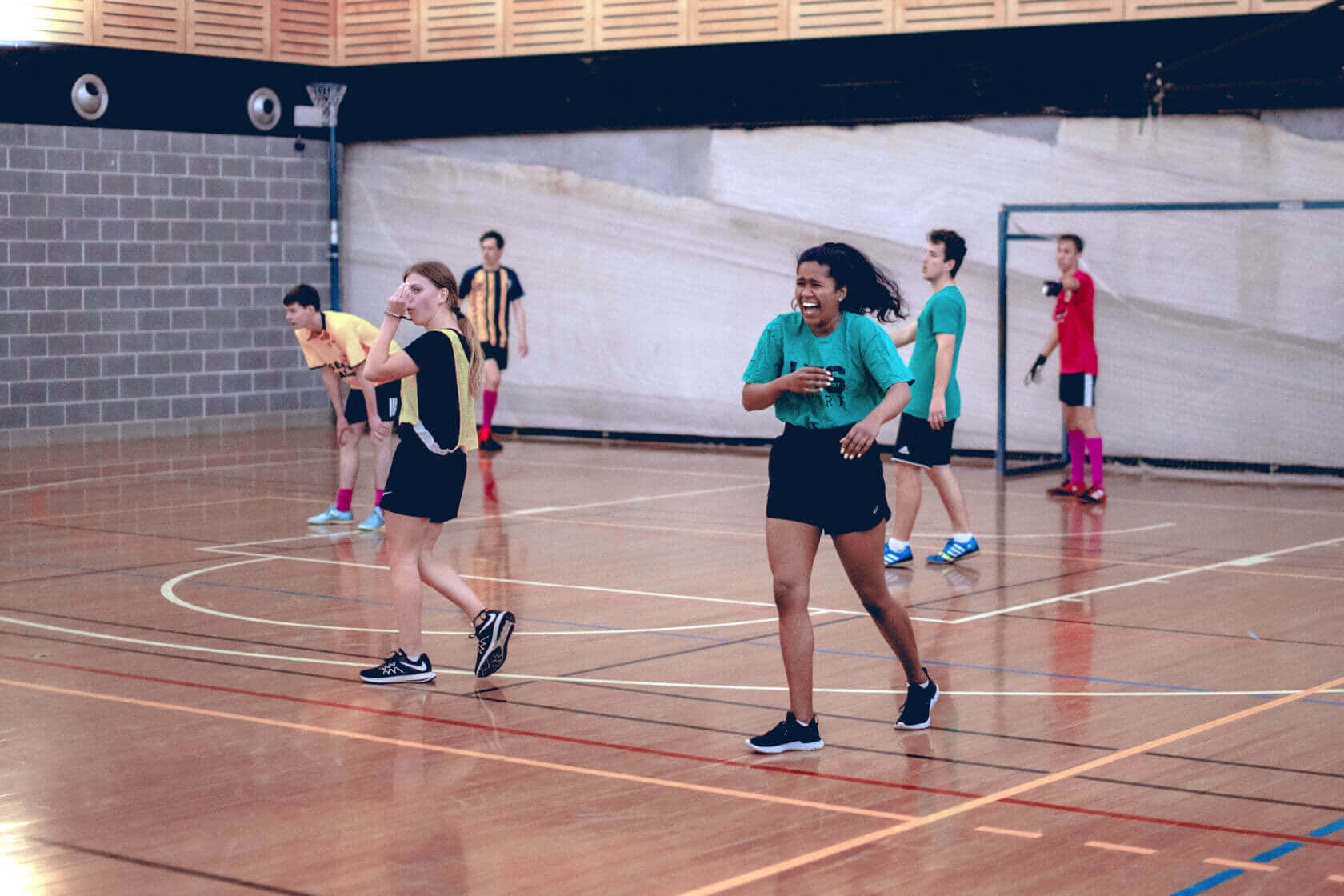 sport 桌布 壁紙 — 年輕運動員在明亮的體育館燈光下，在拋光木地板上笑著進行競技性室內足球比賽。