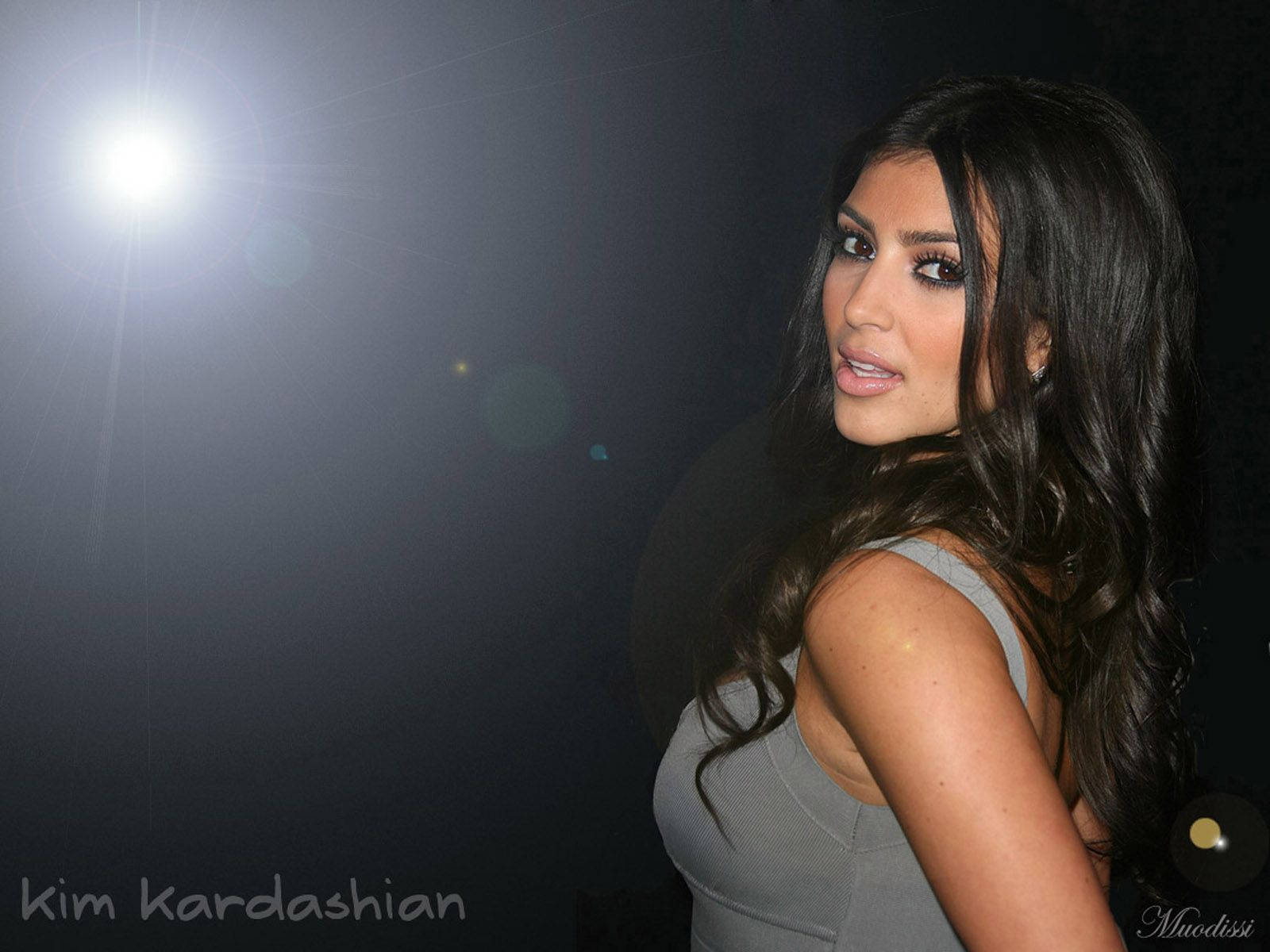 Kim Kardashian 穿著灰色上衣在聚光燈下，帶有鏡頭光暈。