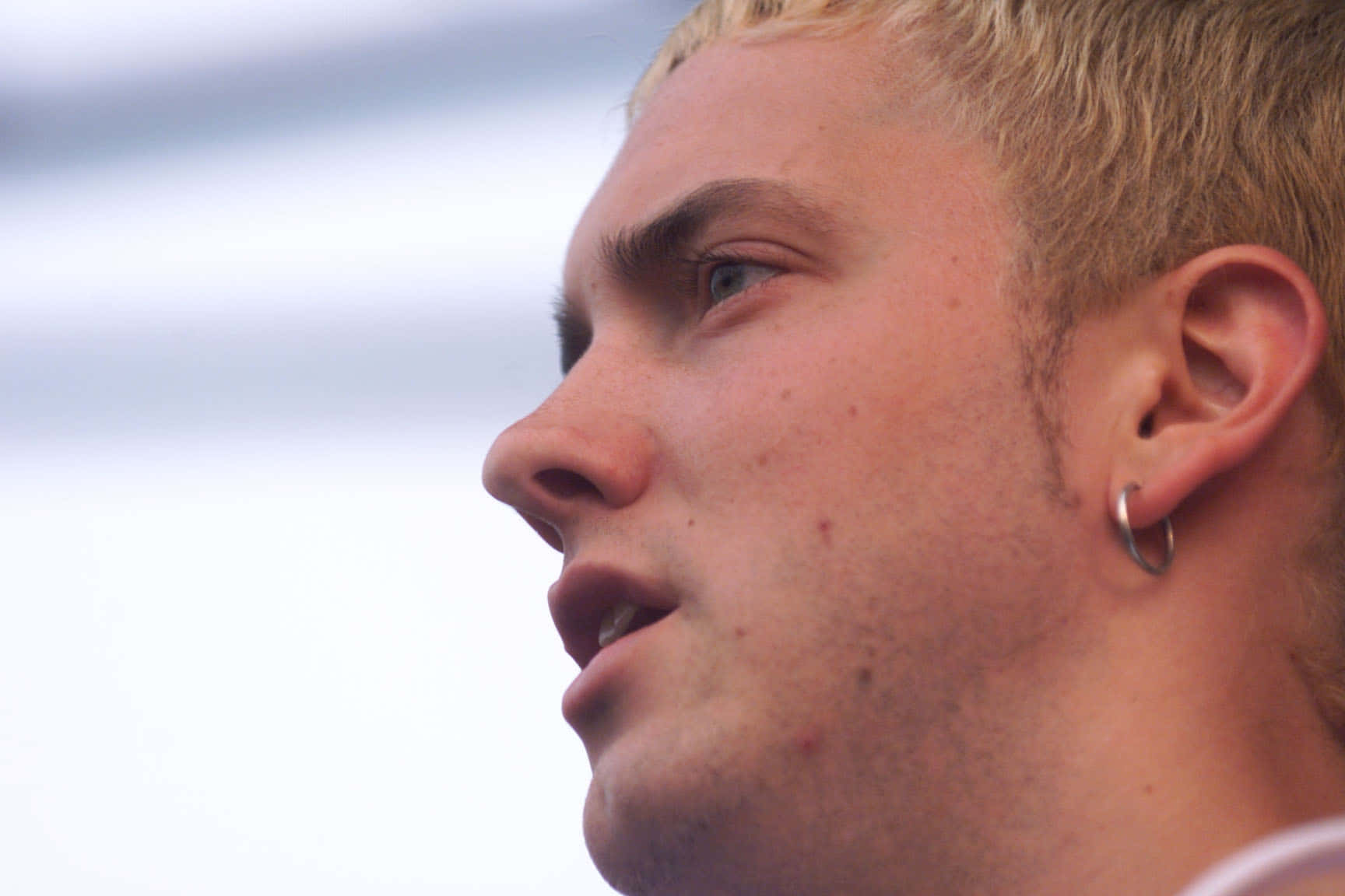 Eminem 桌布 壁紙 — 年輕金髮男子戴著圓環耳環，在模糊的天空背景下沉思地凝視的close-up側面照。