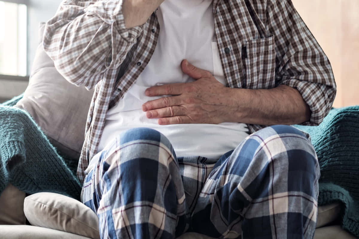 一位穿著格仔睡衣嘅老人家坐喺梳化上，按住腹部。