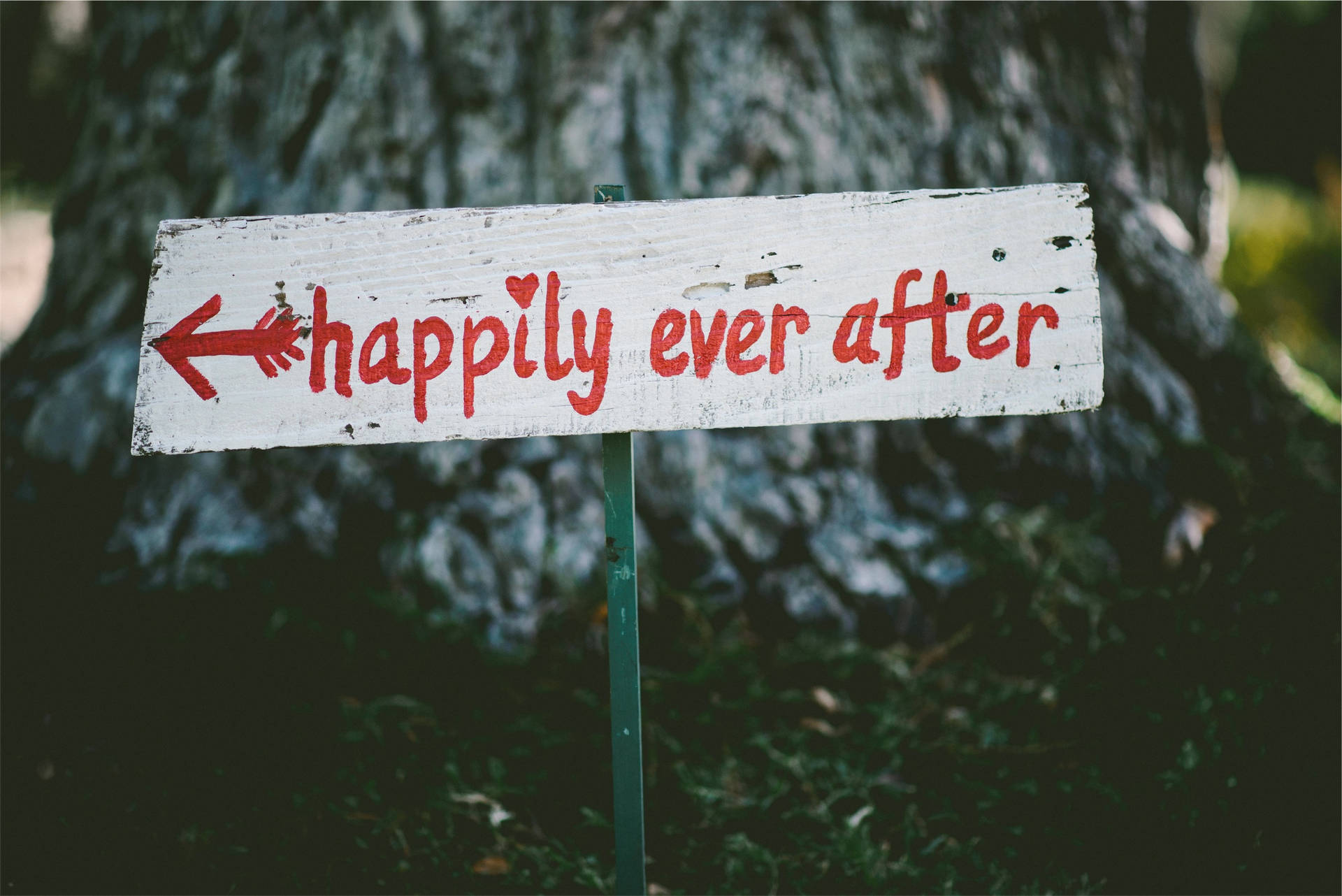 一塊質樸的木牌，上面有紅色文字「happily ever after」，箭頭指向左方。