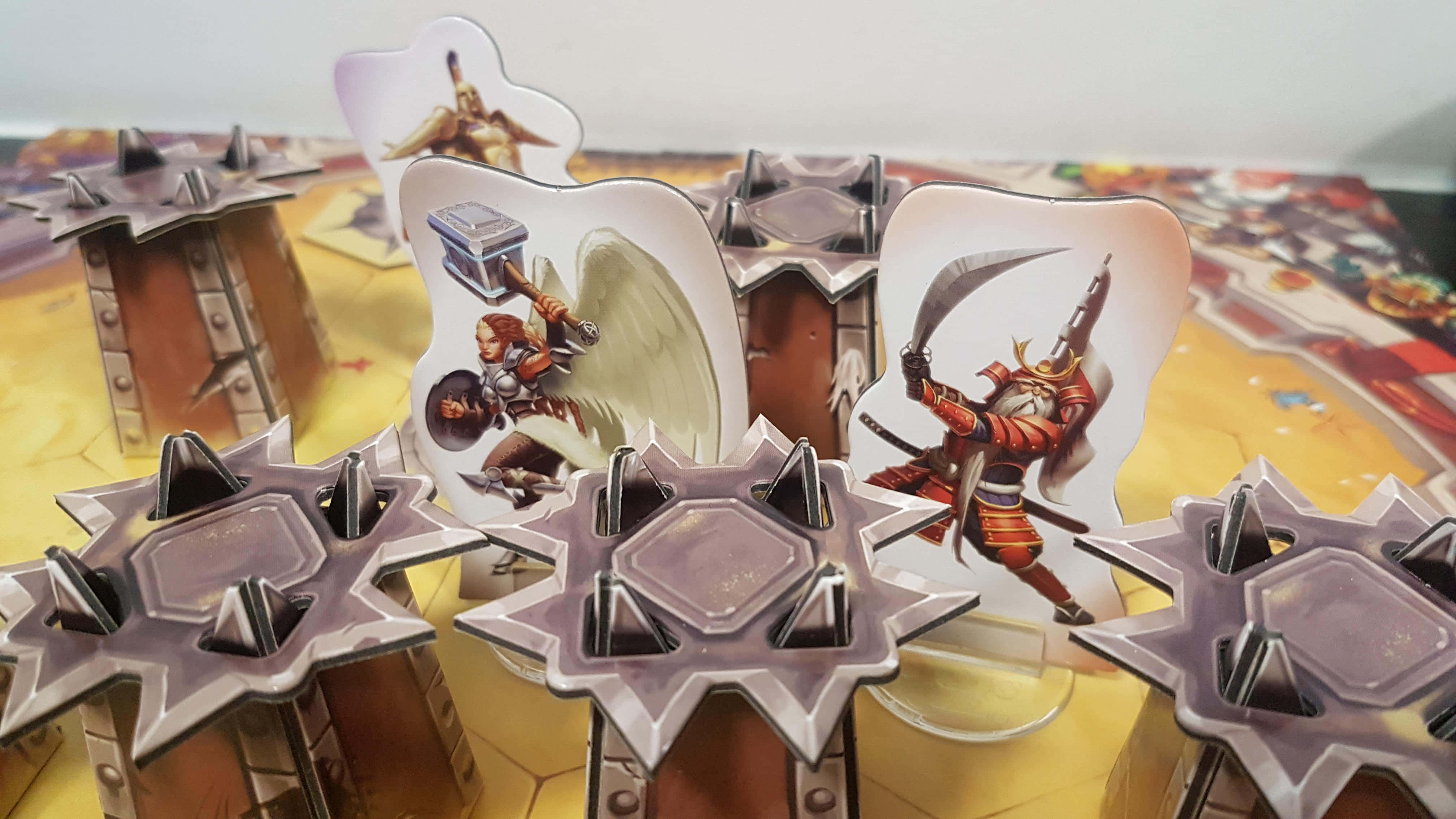 Battle Of Gods 桌布 壁紙 — 幻想主題遊戲棋子的特寫，棋子帶有插圖戰士和尖刺星形底座，放置在色彩繽紛的棋盤上。