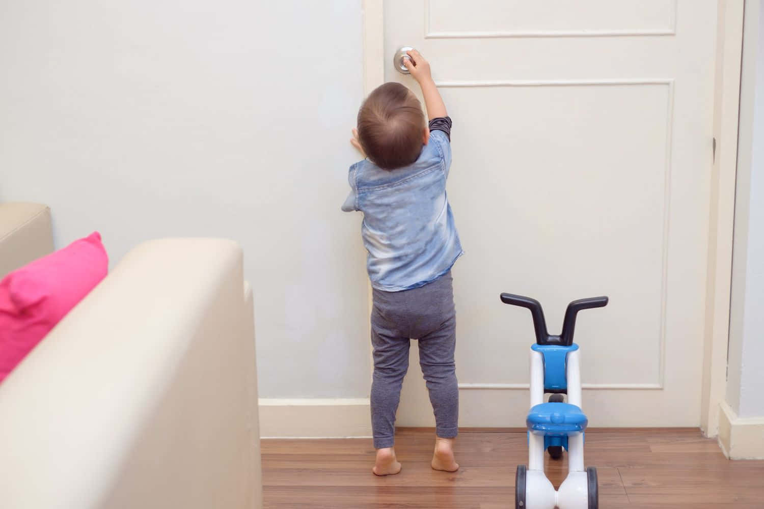 幼兒在室內靠近三輪車和沙發轉動門把手。