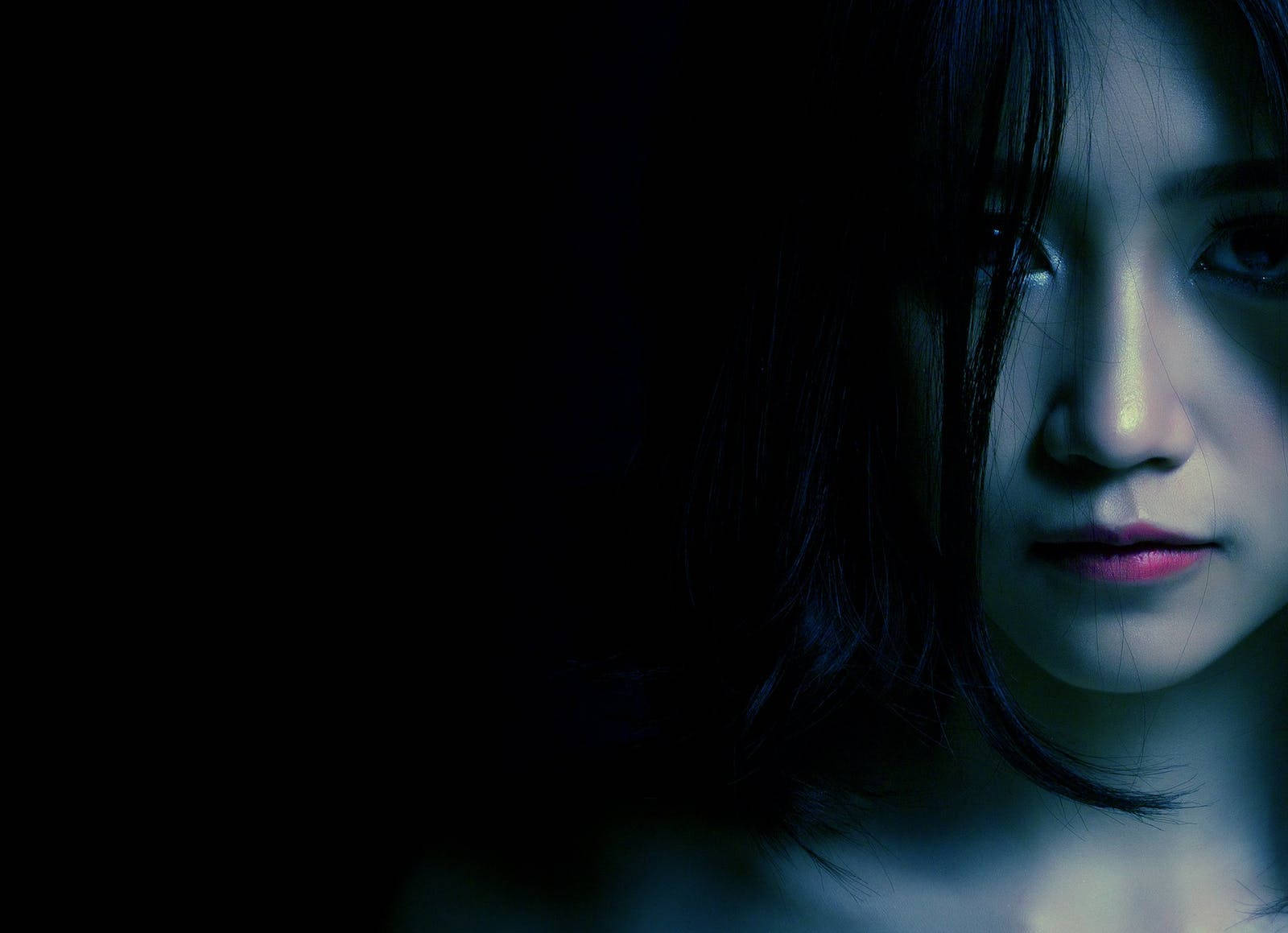 幽暗甜美少女風 壁紙 — 一個女人的臉部在黑暗背景下被冷藍色光線部分照亮，營造出陰鬱而神秘的氛圍。