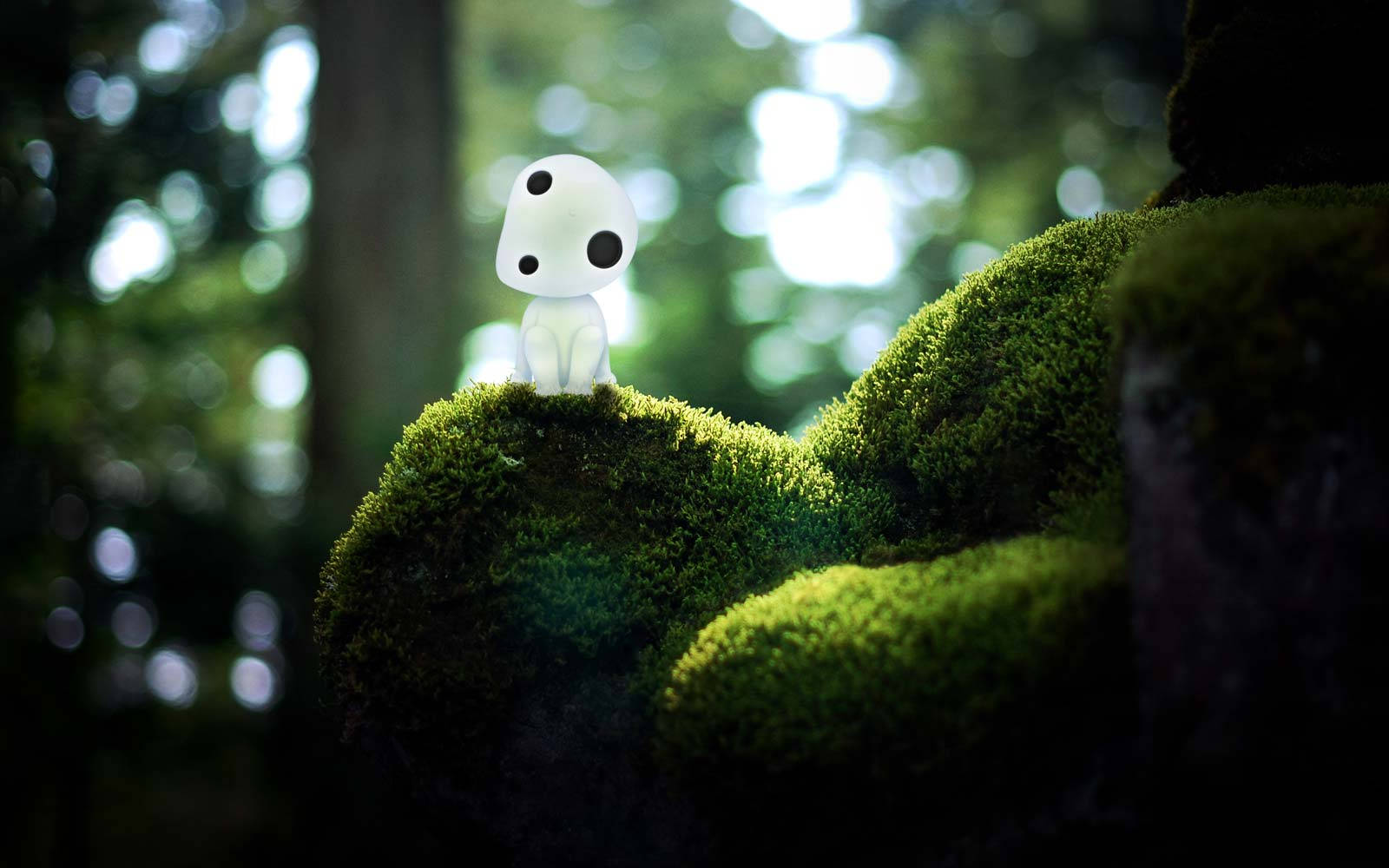 《幽靈公主》中的 kodama 近景 壁紙 — 一個白色的小幽靈狀生物，黑色眼睛，棲息在陽光斑駁的森林中一塊茂密的綠色苔蘚岩石上。