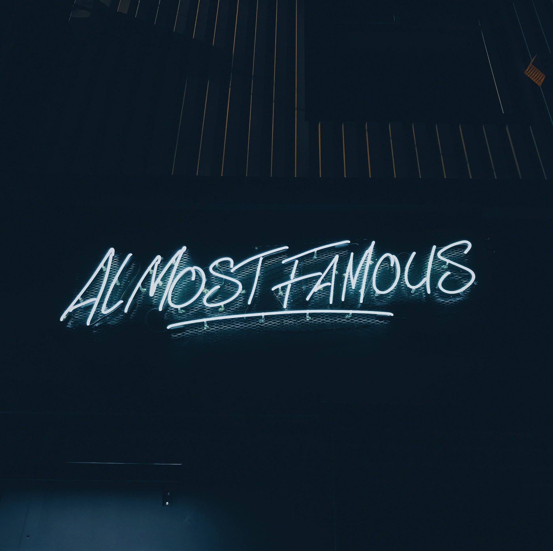 霓虹燈牌寫著「Almost Famous」，在黑暗的牆壁上發出藍光。