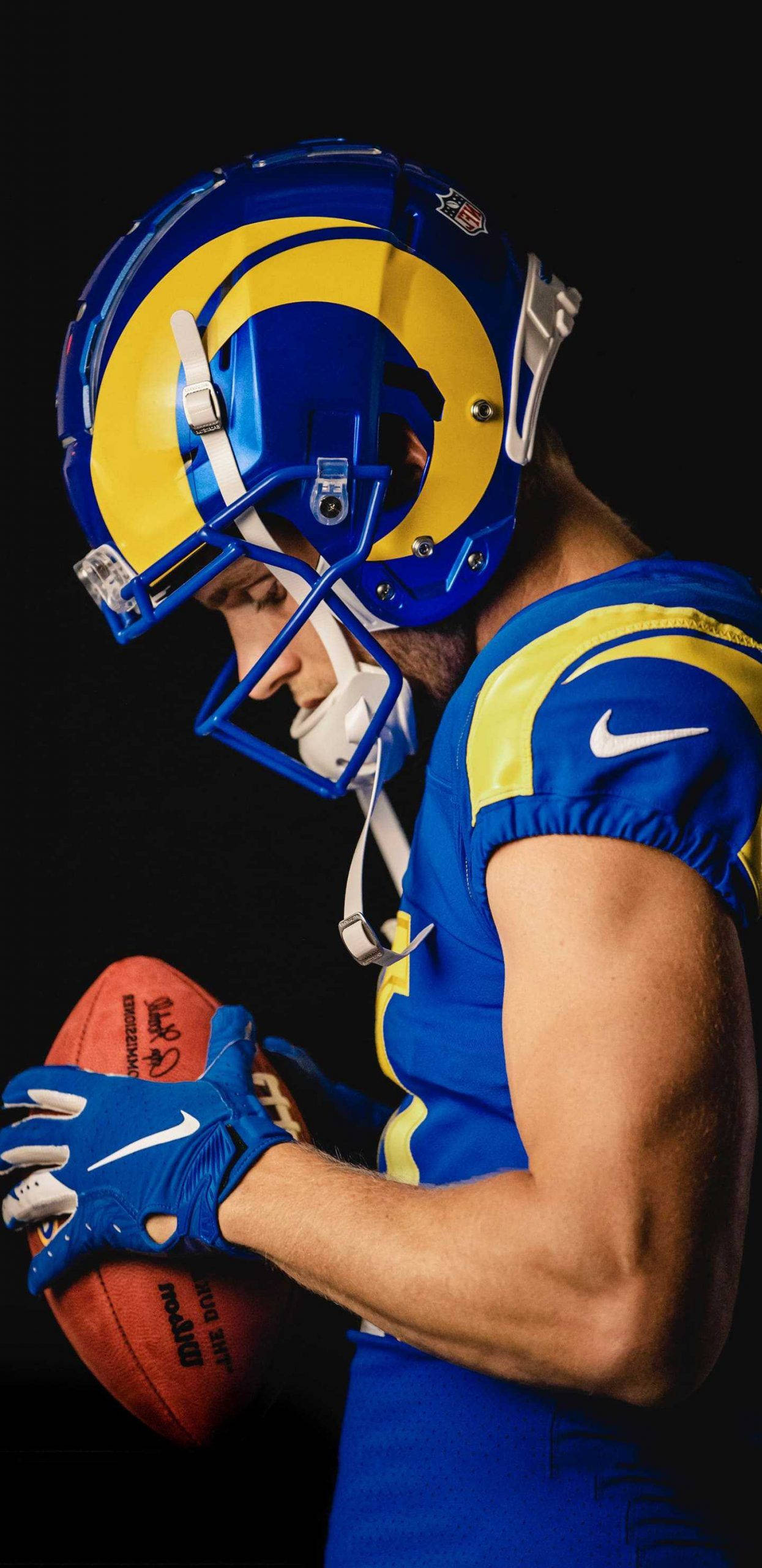 庫珀·庫普 NFL 洛杉磯公羊隊攝影寫真 壁紙 — 一名身穿藍黃裝備的美式足球員在黑色背景前，在戲劇性燈光下抱著球。