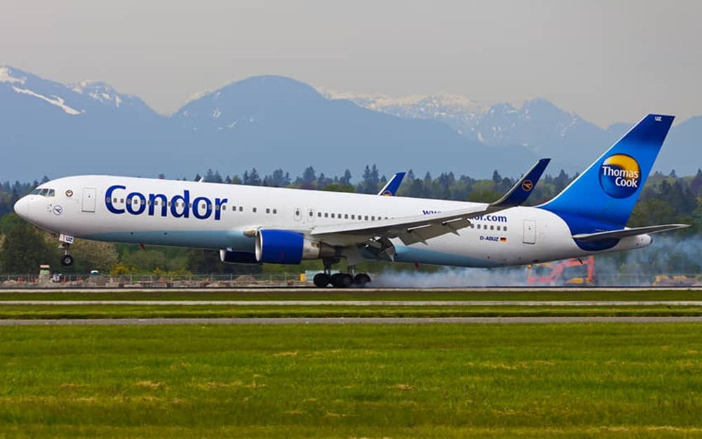 Condor Thomas Cook飛機在跑道上，背景有山脈和綠色田野。