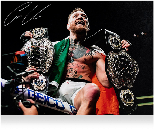 康納·麥格雷戈冠軍慶祝 壁紙 — Conor McGregor 在八角籠中勝利慶祝，手持兩條冠軍腰帶，肩上披著綠色和橙色的布。