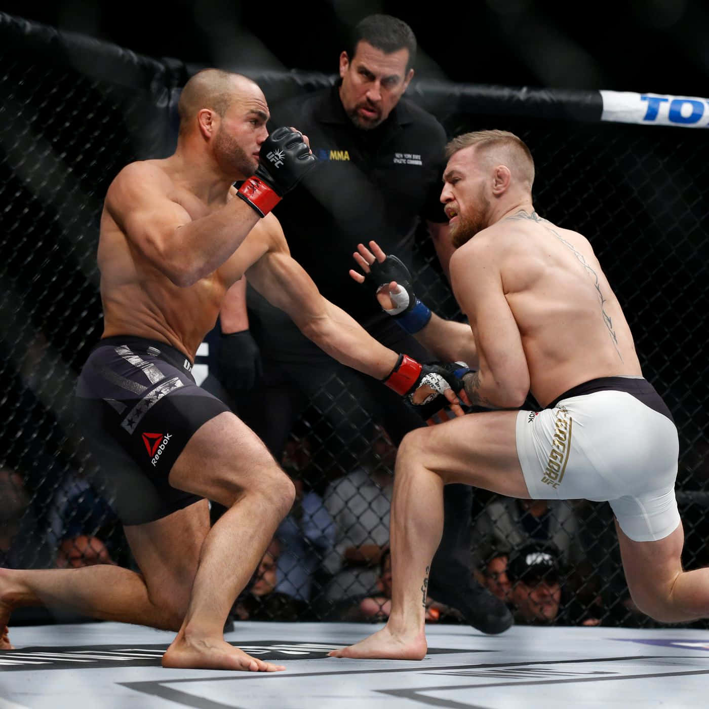 兩名男性拳手戴著MMA手套和短褲在八角籠內扭打。