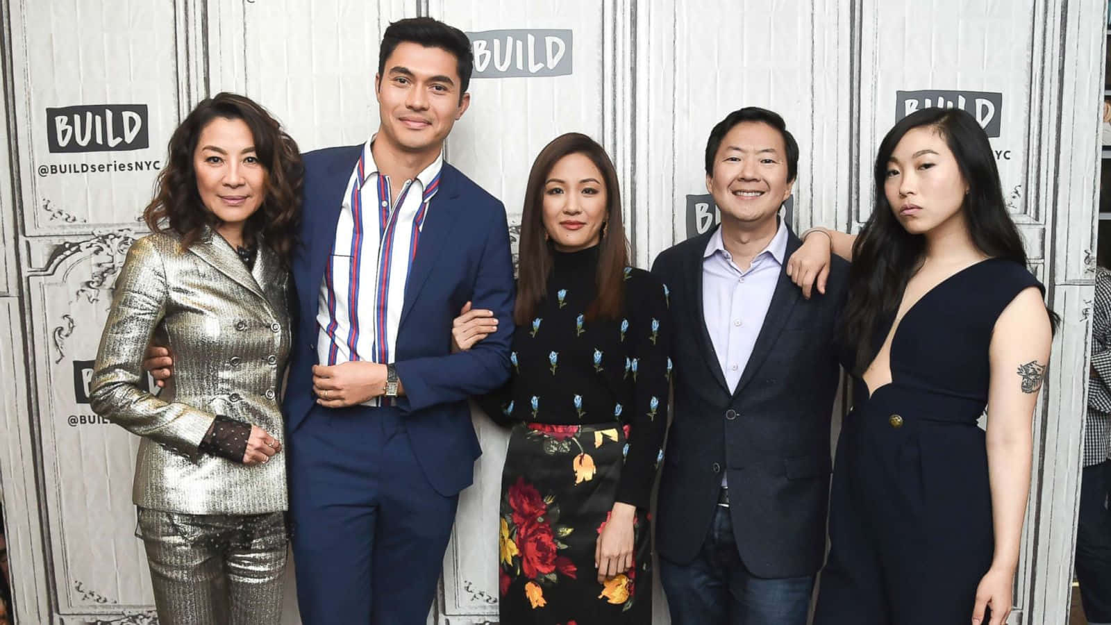 五位穿著正式服裝的人在BUILD活動中擺姿勢，背景為品牌背景。