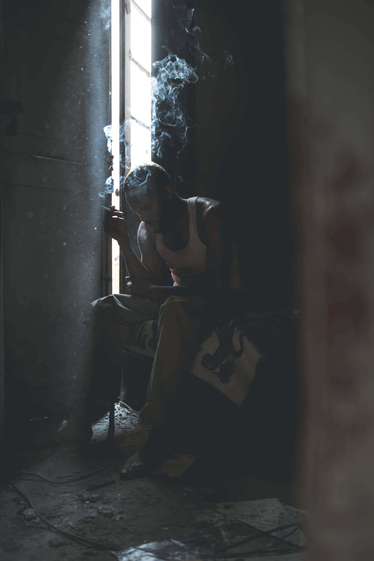一個男人在昏暗的房間裡靠窗抽煙。