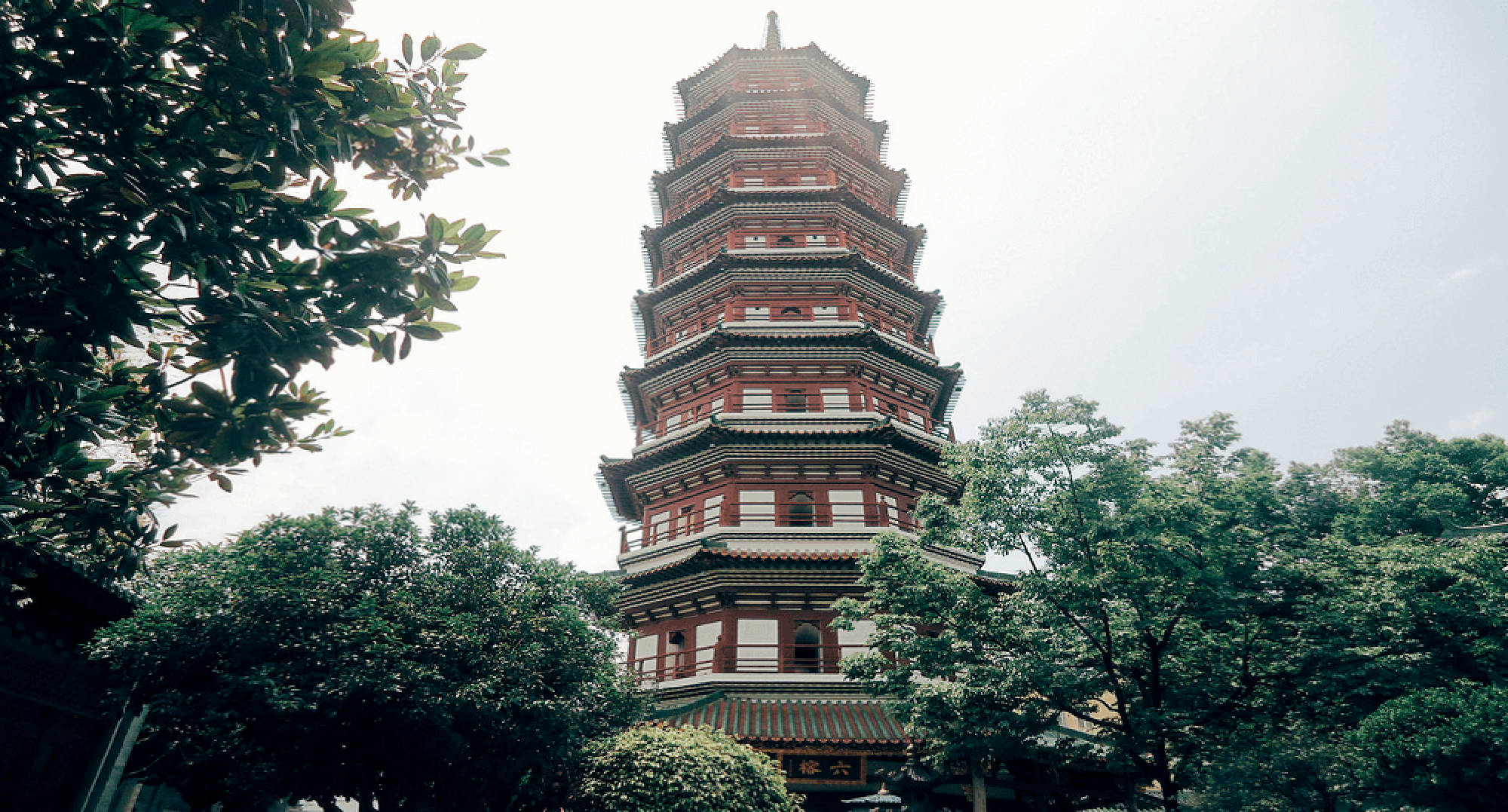 廣州六榕寺 壁紙 — 一座高聳的傳統中式寶塔在陰天中從茂密的綠樹中升起。