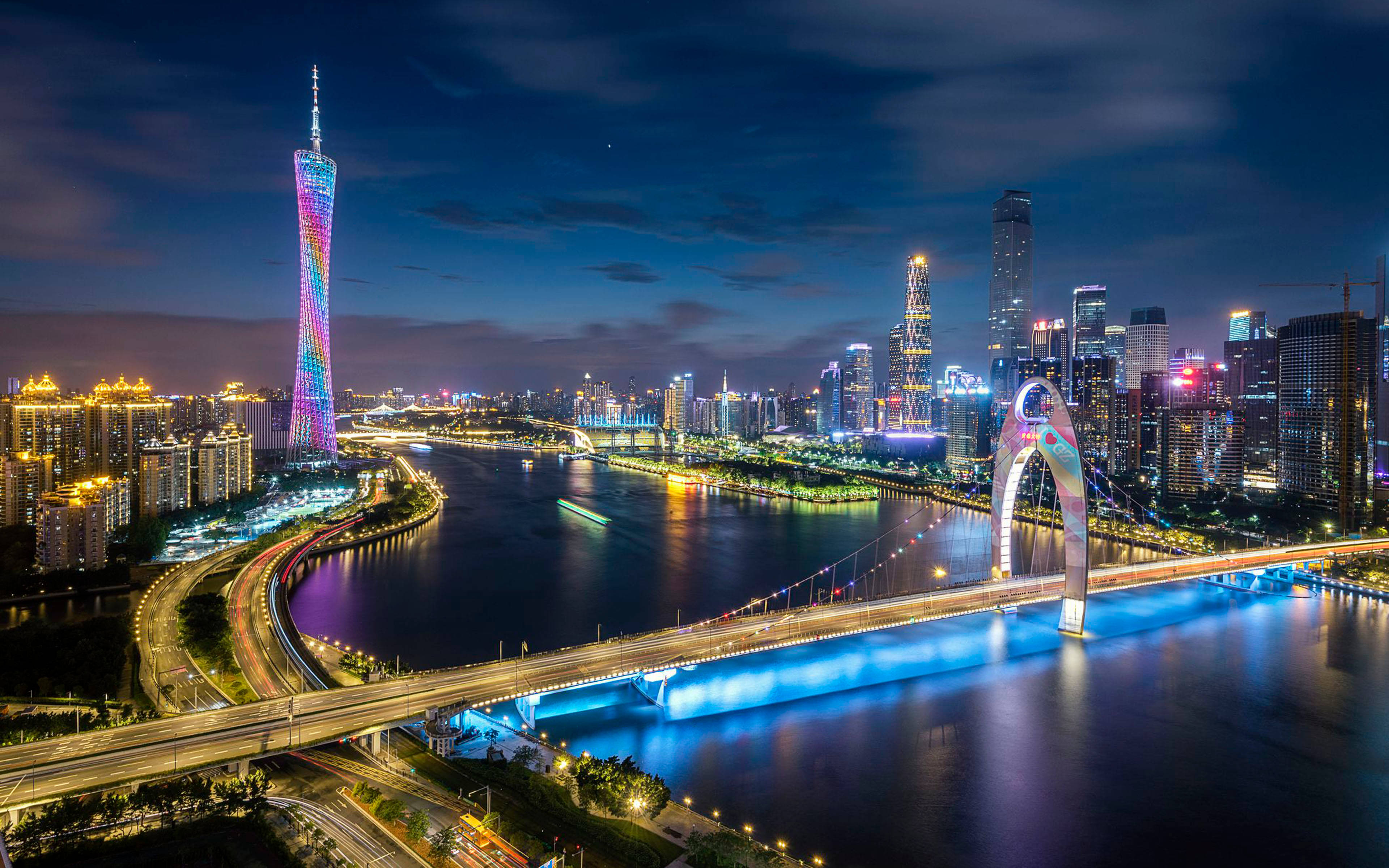 廣州夜景 壁紙 — 一個耀眼的夜間城市景觀，特色是發光的塔樓和橫跨河流的照明橋樑，帶有交通痕跡。