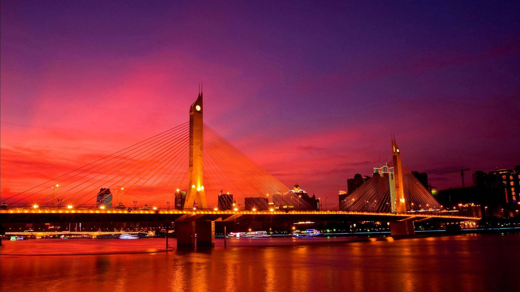 廣州海印大橋 壁紙 — 一座現代斜拉橋在平靜的河面上，以溫暖的燈光映襯著火紅的日落天空。