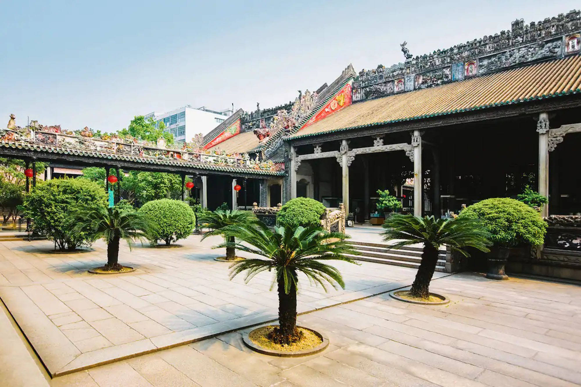 廣州陳家祠 壁紙 — 一個傳統中式寺廟庭院，擁有華麗的瓦頂和盆栽蘇鐵，在明亮的日光下。