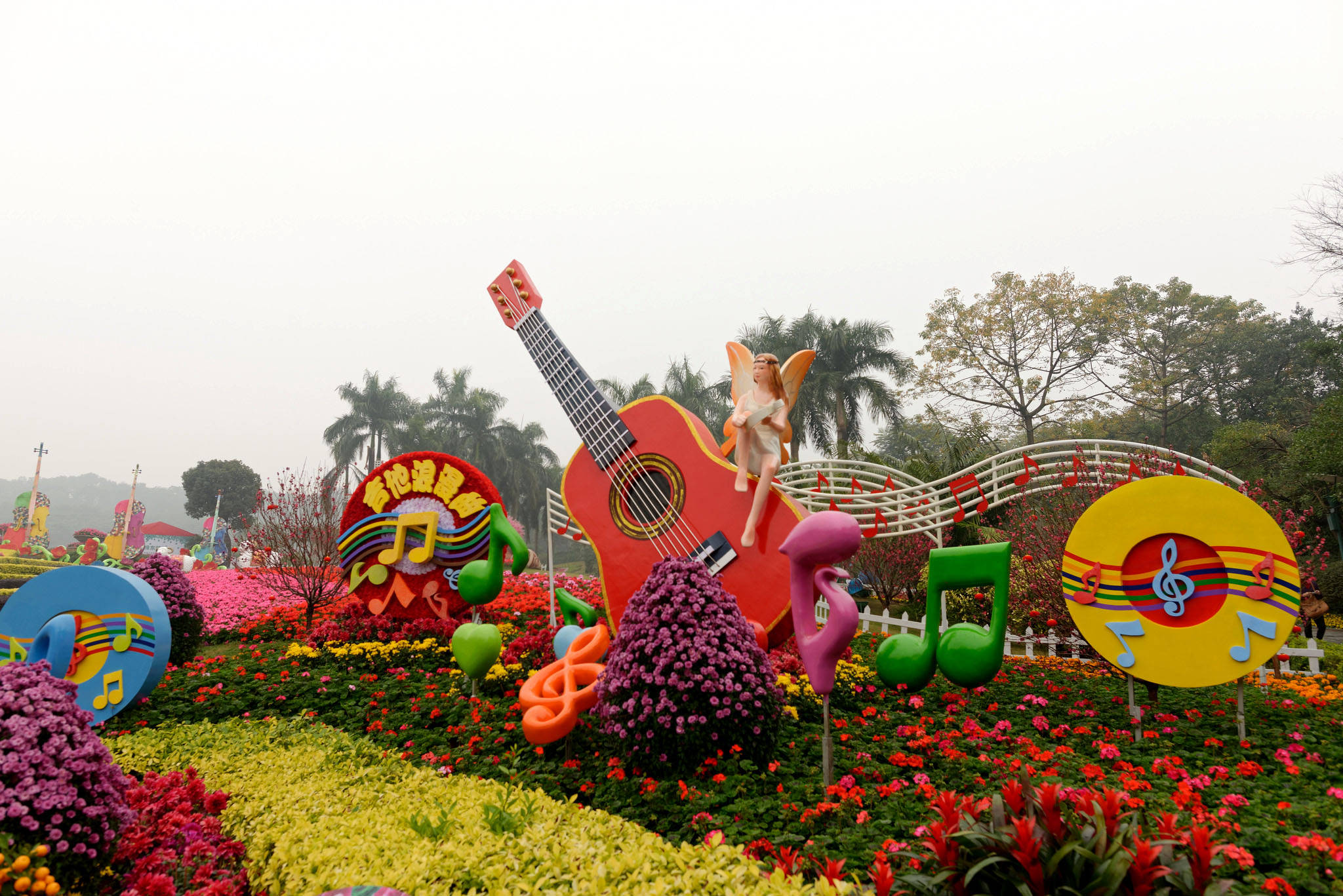 廣州雲台園 壁紙 — 一個充滿活力的花卉展示，特色是巨大的彩色音符和一把紅色結他，上面棲息著一個小仙女，周圍是盛開的花朵。