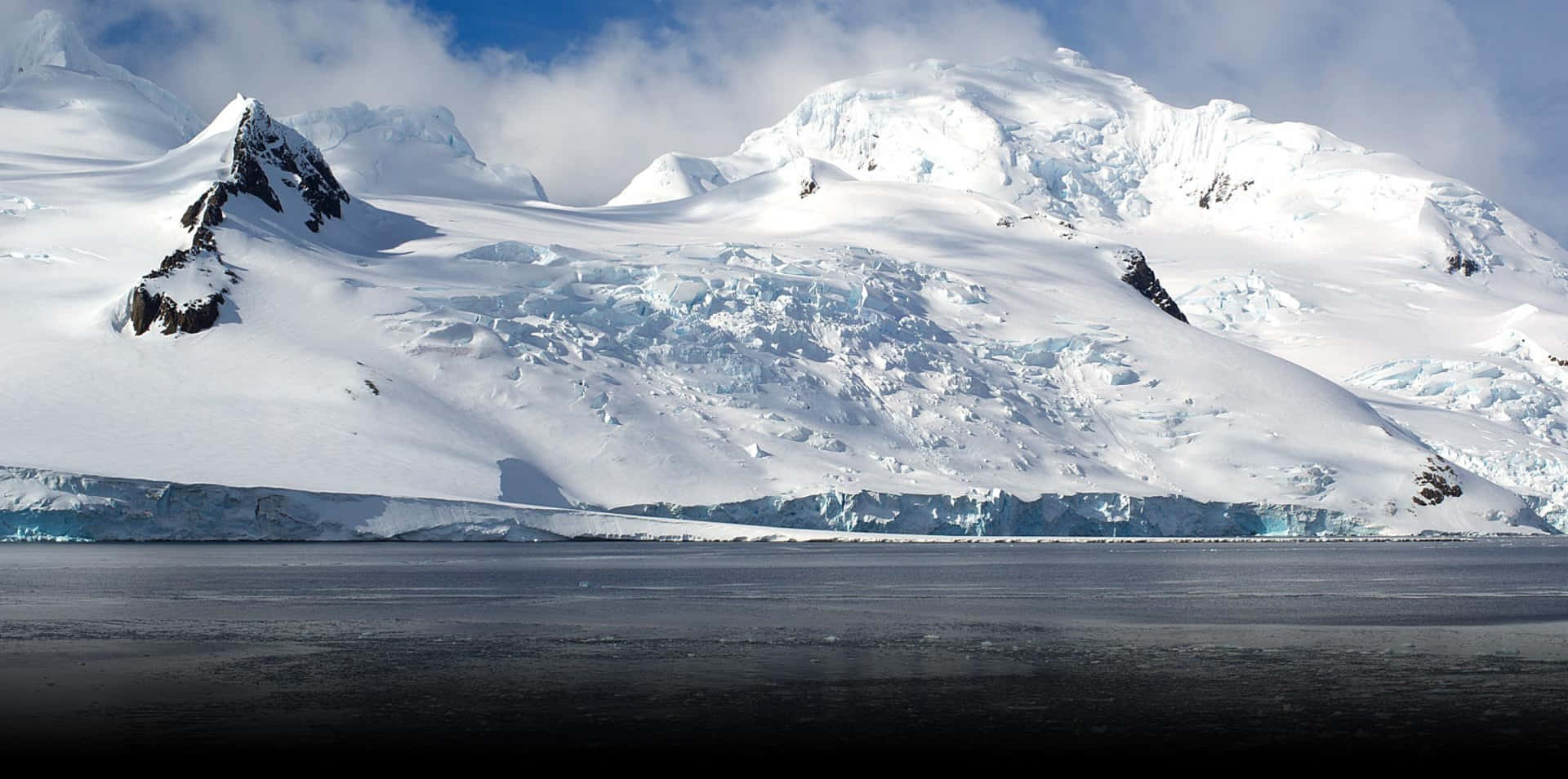 Antarctica 桌布 壁紙 — 廣闊冰川在明亮藍天與薄雲下崩解落入暗海。