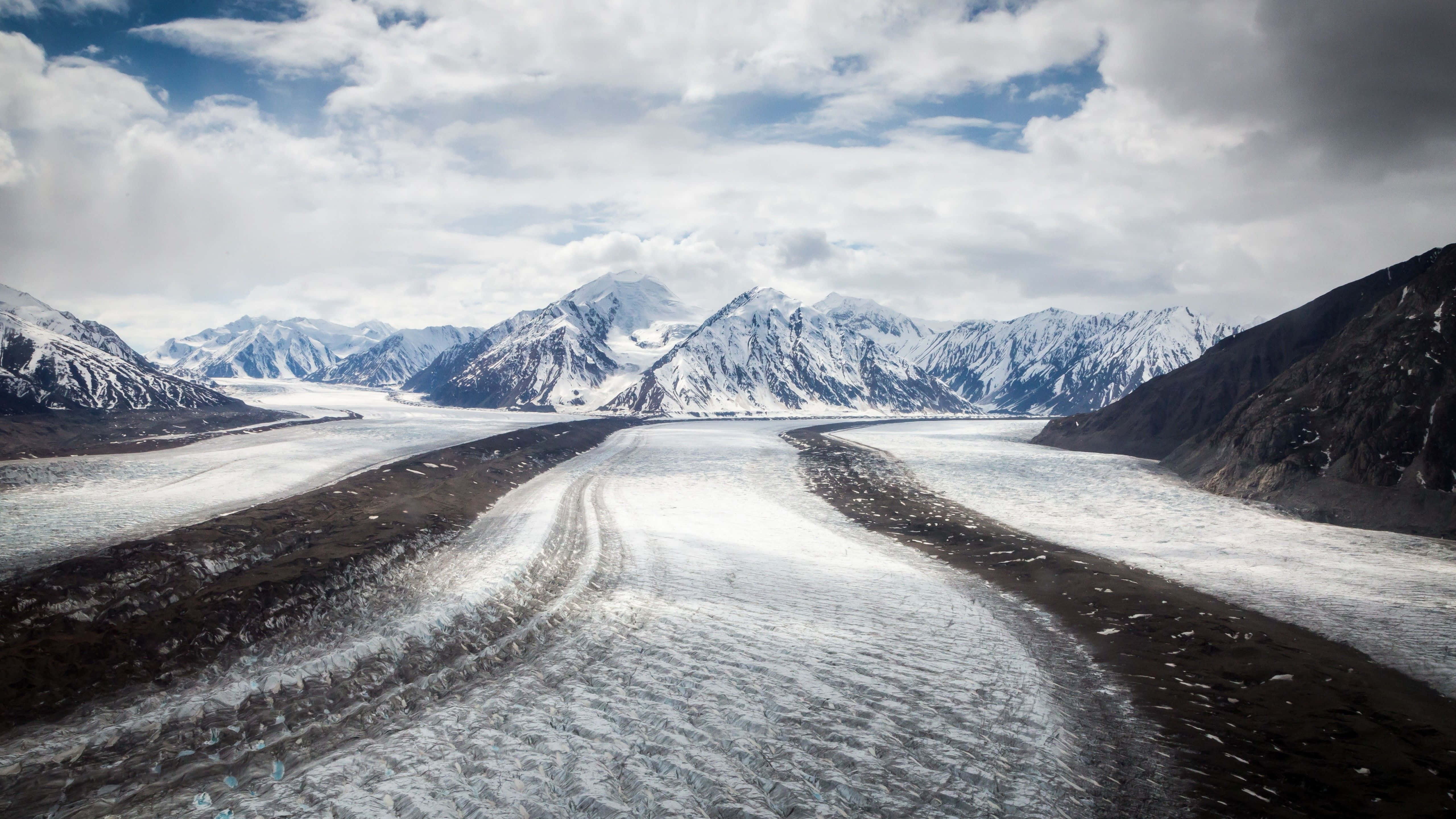 Icy Road 桌布 壁紙 — 廣闊嘅冰川喺戲劇性嘅多雲天空下蜿蜒穿過崎嶇嘅山谷。