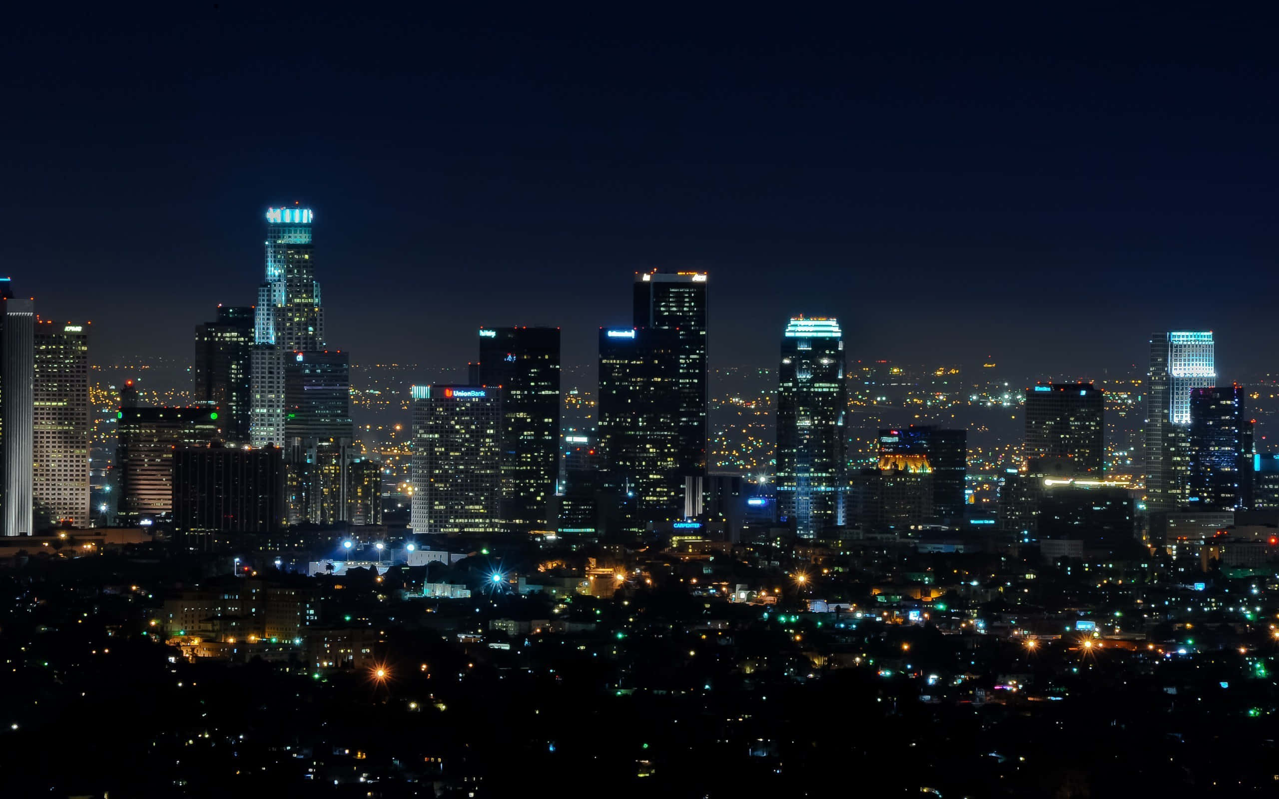 La 桌布 壁紙 — 廣闊城市景觀的 panoramic 夜景，高聳的摩天大樓在黑暗的天空中閃耀。