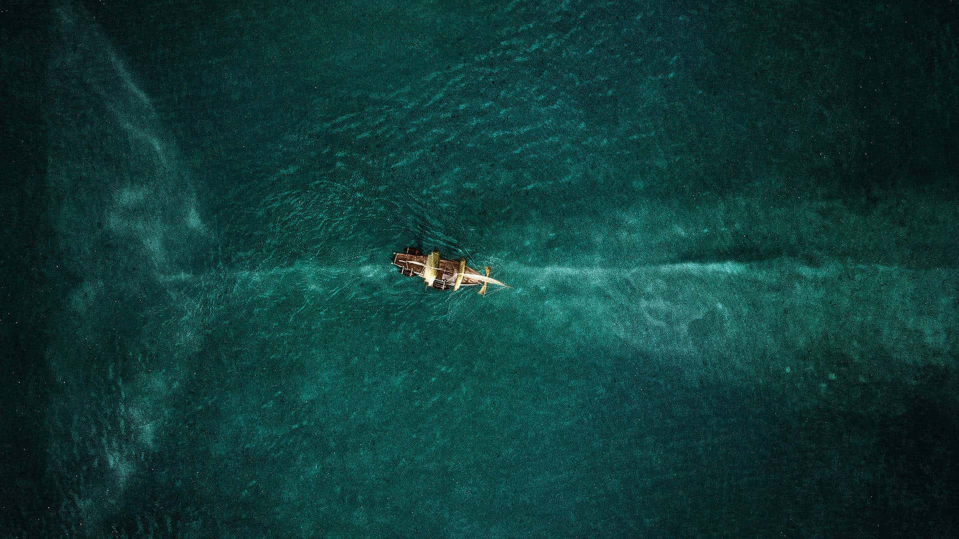 廣闊海洋的寧靜之美 壁紙 — 從空中俯瞰一艘小木船劃過碧綠的海水，留下一道白色的航跡。